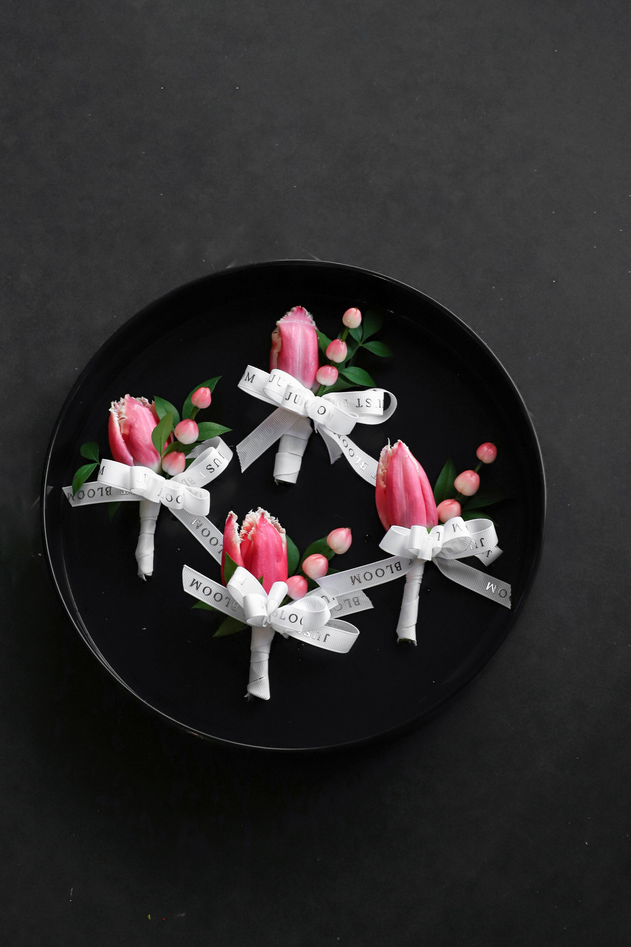 Close-up of four Boutonnieres on a black tray by Just Bloom Hong Kong, showcasing pink fringed tulips and hypericum berries with Just Bloom white ribbon