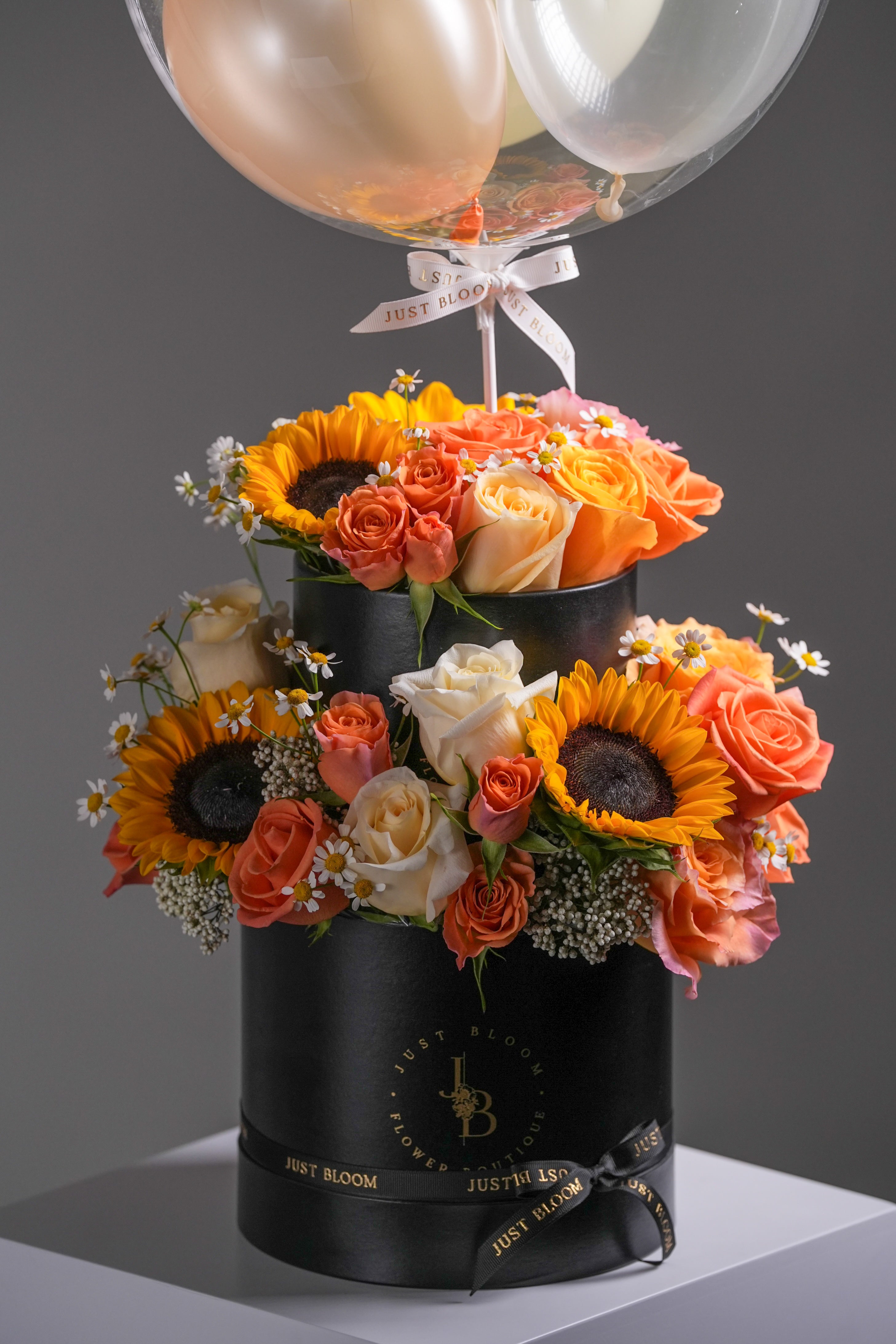 Sunny balloon flower box featuring yellow sunflowers, cream roses, and orange roses in a black hatbox