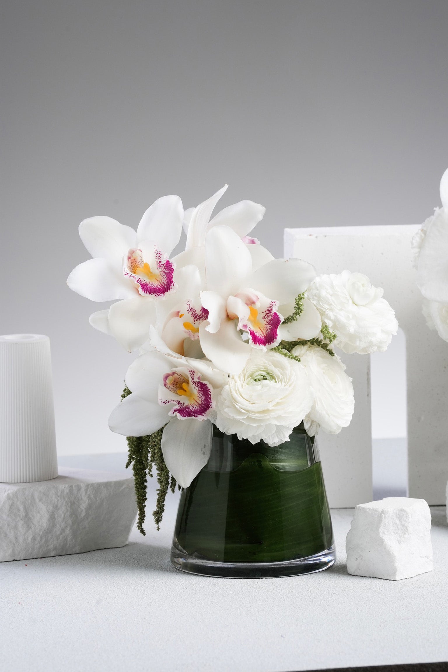 Just Bloom Faye small vase floral gift featuring white orchids and ranunculus with glass vase – styled on table