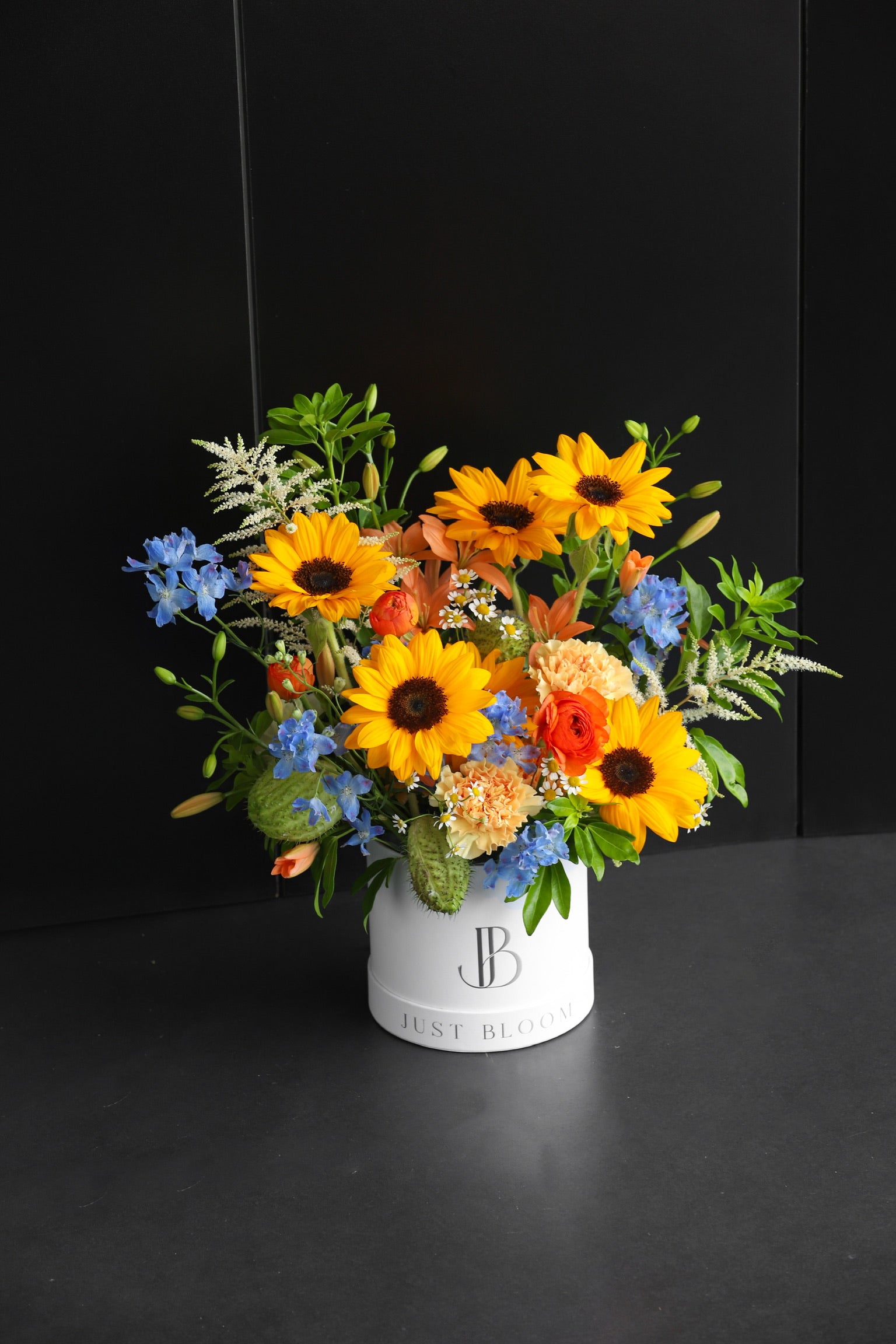 Bold warm-toned fresh flower box arrangement with sunflowers and mixed seasonal blooms in a white Just Bloom hat box against a dark background — Just Bloom Hong Kong