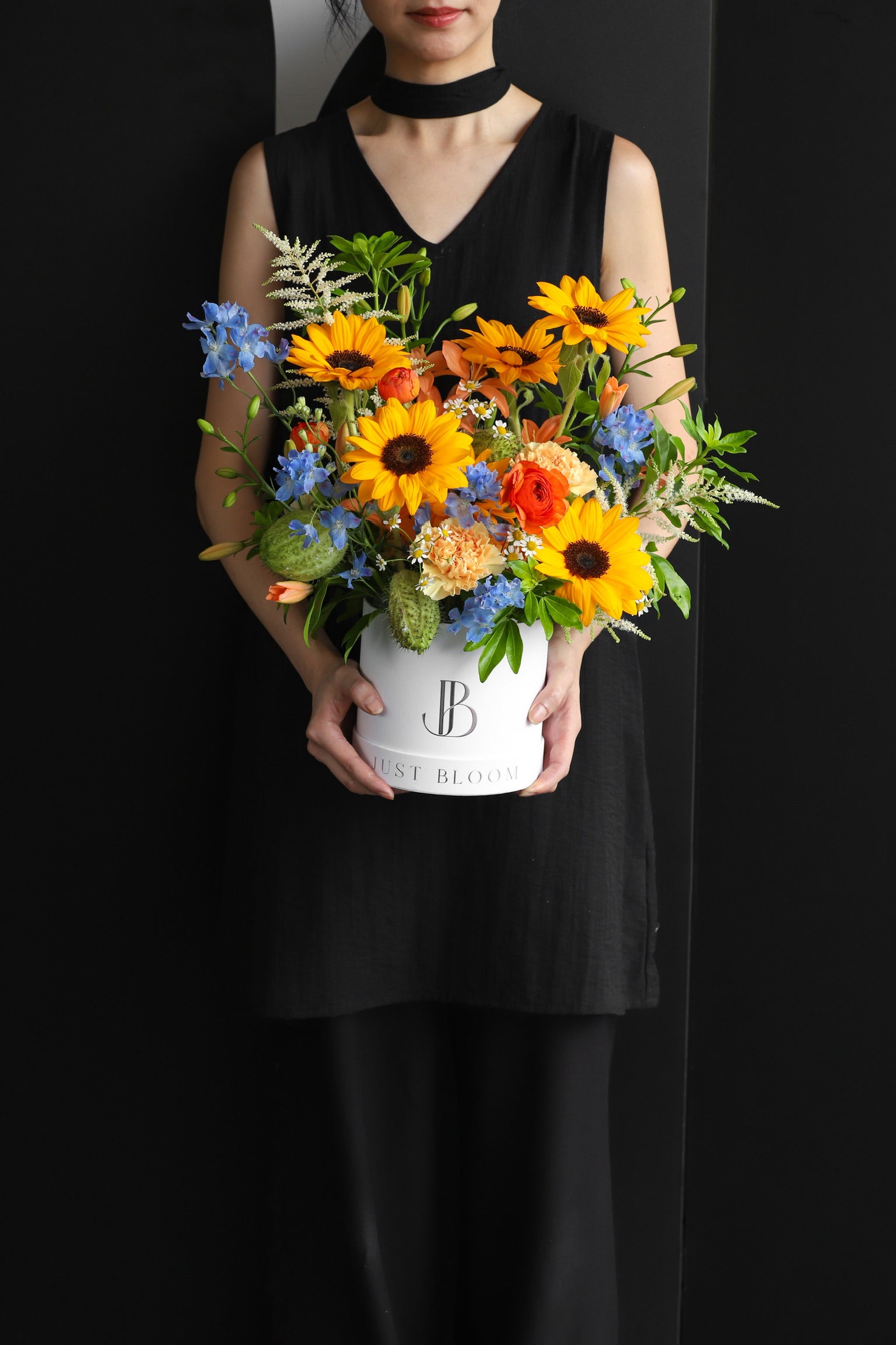 Model holding a bold warm-toned flower box arrangement with sunflowers and mixed seasonal blooms in a white Just Bloom hat box — Just Bloom Hong Kong