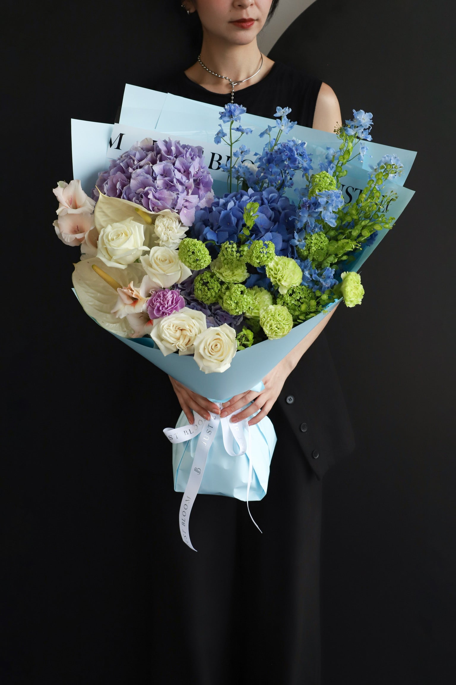 Model holding an oversized fresh flower bouquet in cool blue and purple tones wrapped in Just Bloom sky blue paper against a dark background — Just Bloom Hong Kong