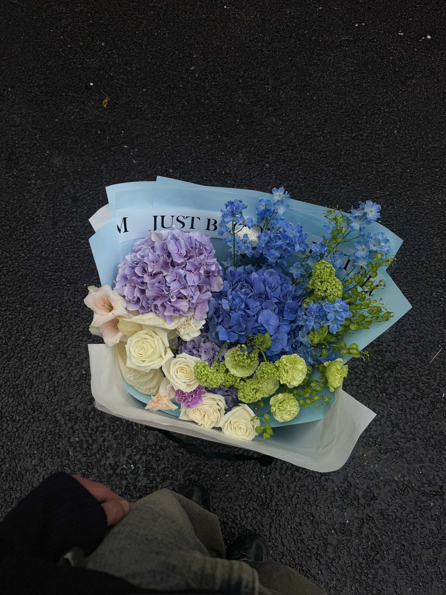 Overhead view of a large cool-toned fresh flower bouquet with blue, purple, and green blooms wrapped in Just Bloom packaging — Just Bloom Hong Kong