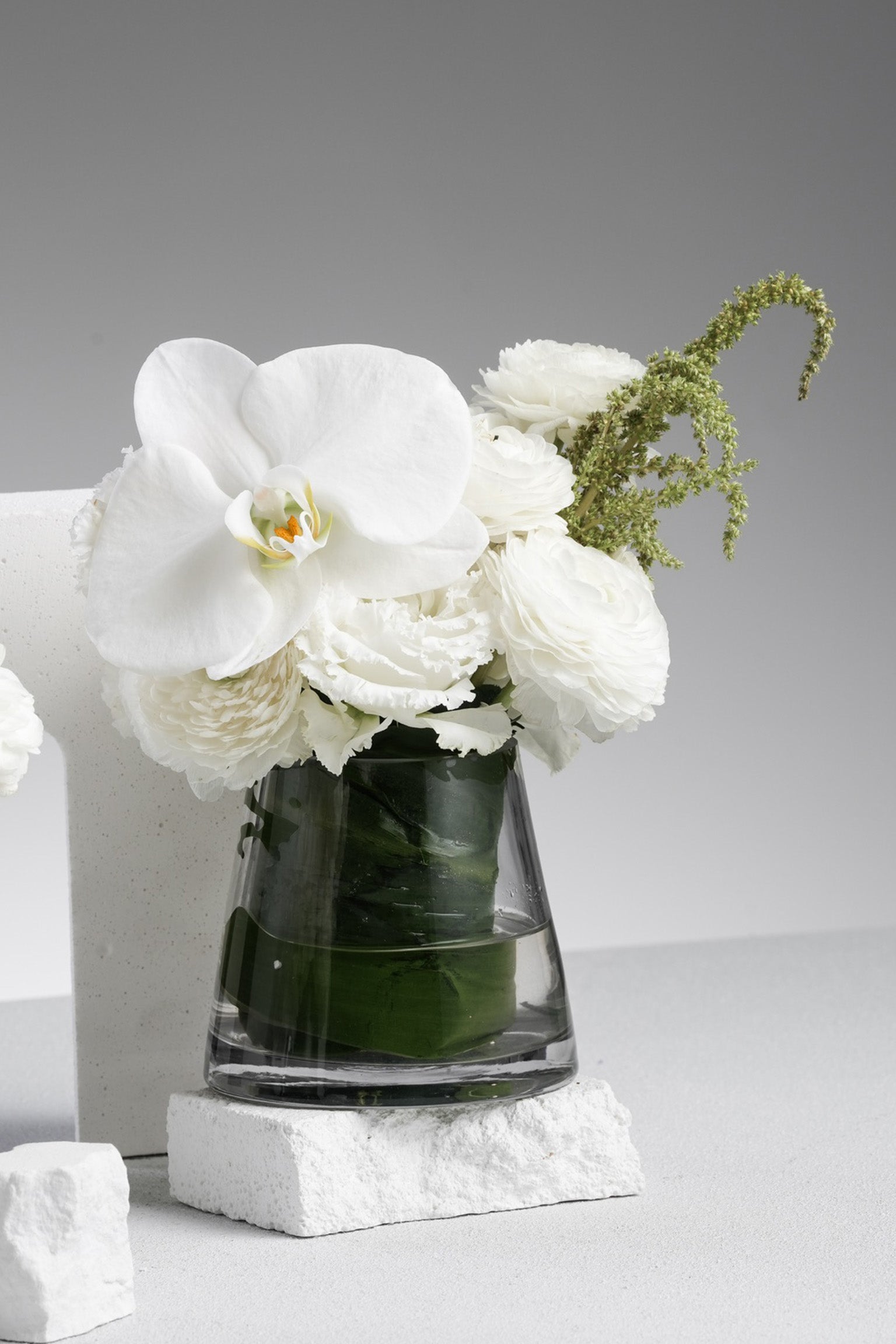 Allyson - A refined mini vase arrangement with white phalaenopsis orchid, ranunculus, and seasonal greens in a clear glass vase. Designed for minimal elegance. Available for same-day delivery in Hong Kong by Just Bloom.
