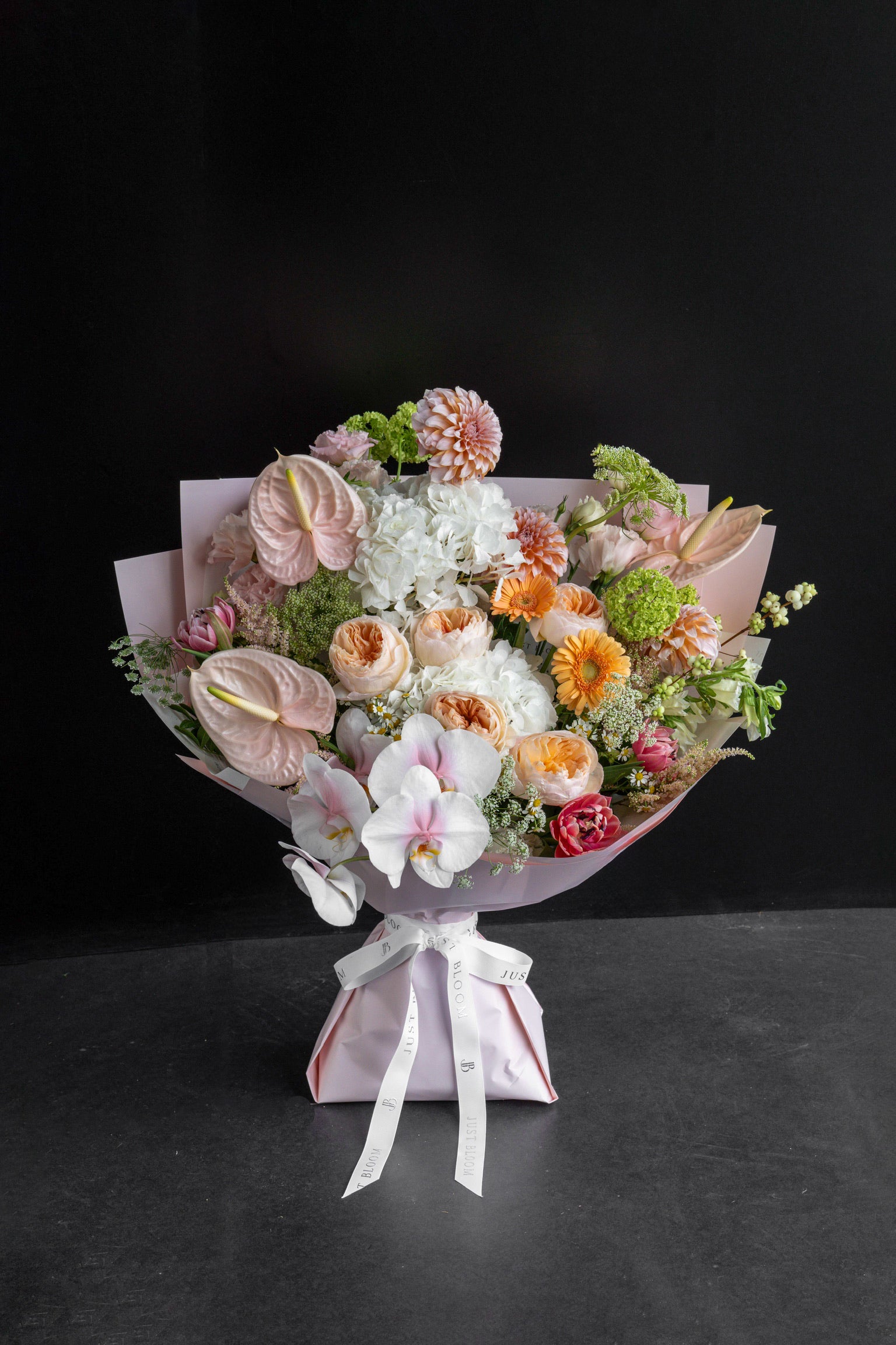 Apricot Garden bouquet of peach, white, and pink blooms wrapped in pink paper against a black backdrop — Just Bloom Hong Kong