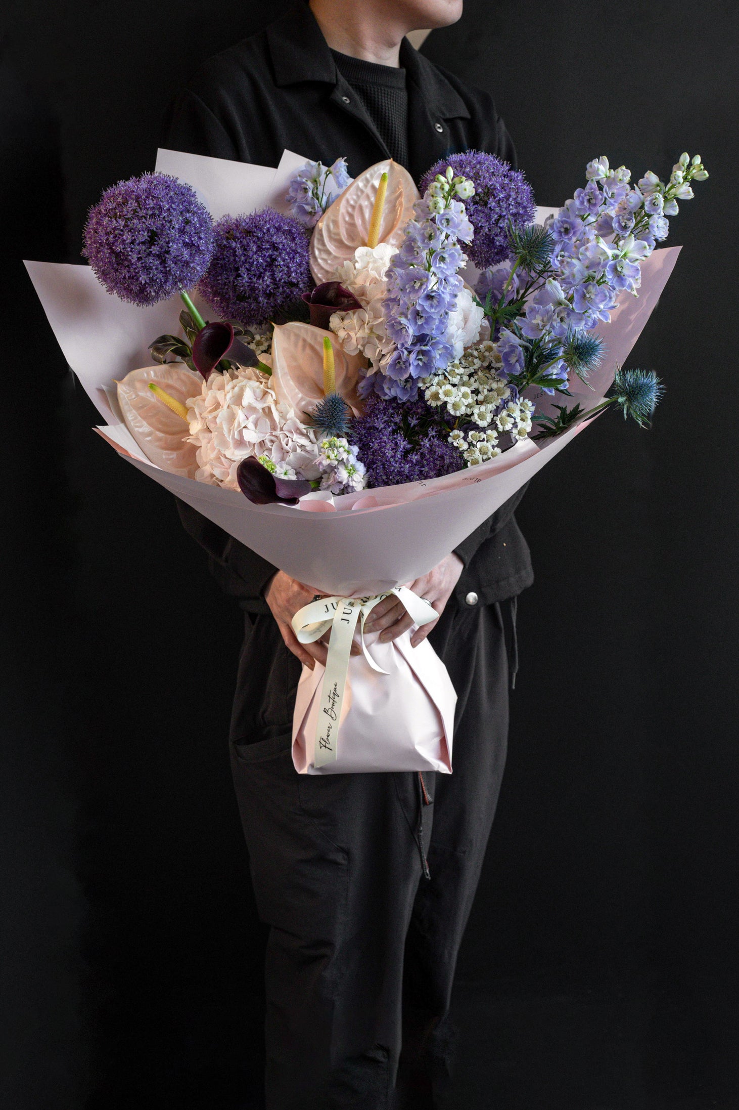 Person in black holding the Lavender Muse bouquet of purple, plum, and blush blooms against a black backdrop — Just Bloom Hong Kong