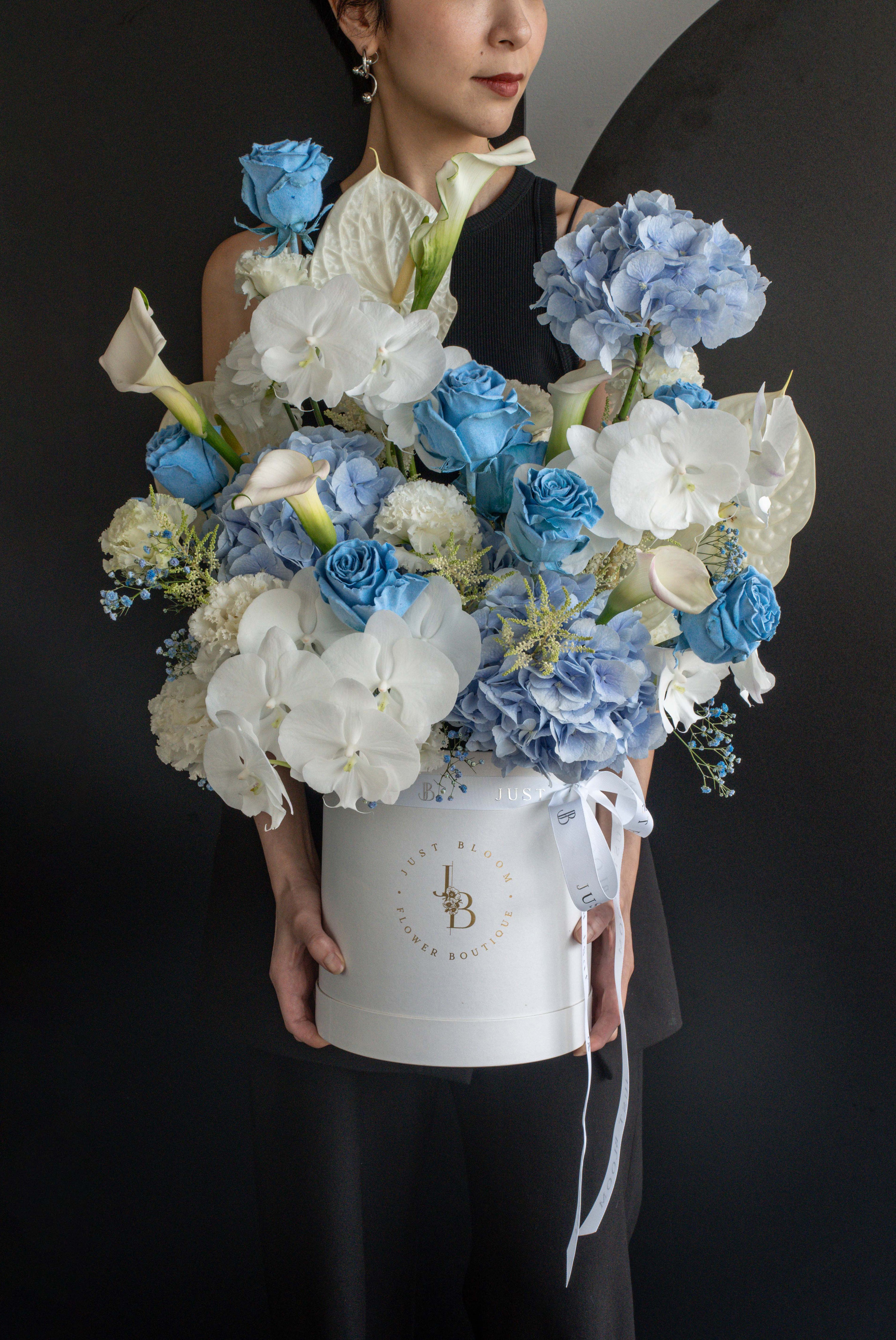 Model holding a blue and white flower box arrangement with tall blooms and rounded clusters against a black backdrop — Just Bloom Hong Kong