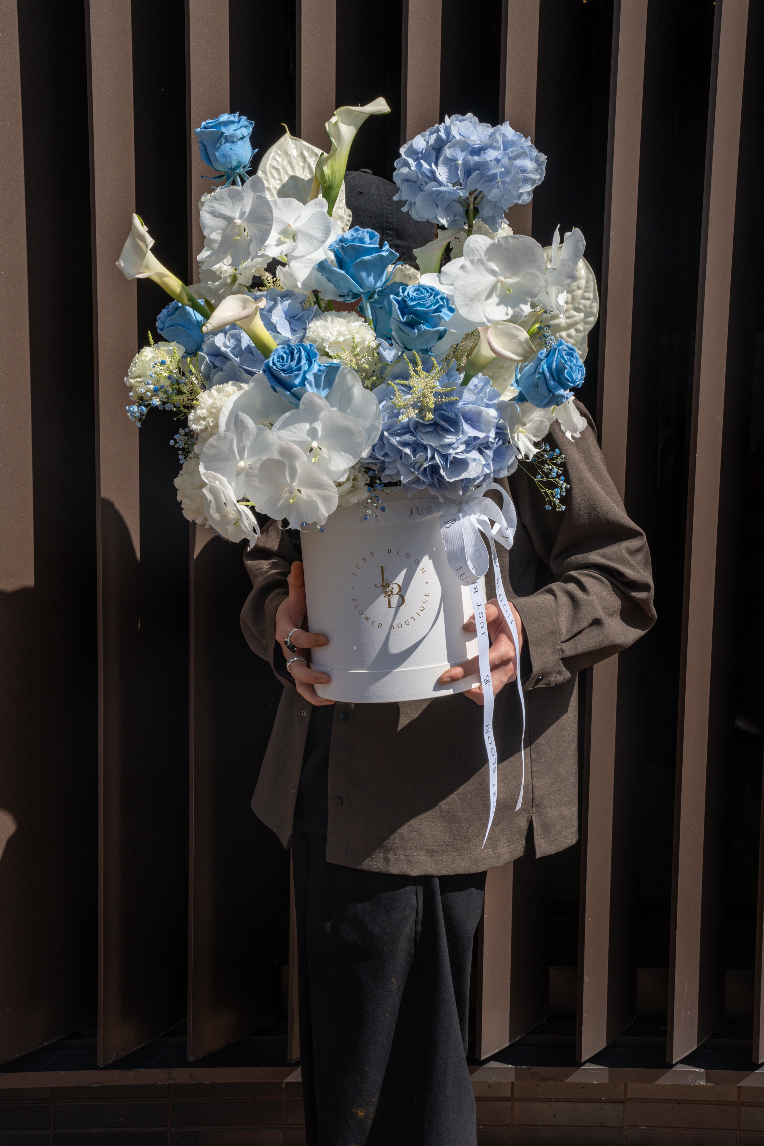 Person holding the Blue Rhapsody flower box outdoors against a slatted wall backdrop — Just Bloom Hong Kong