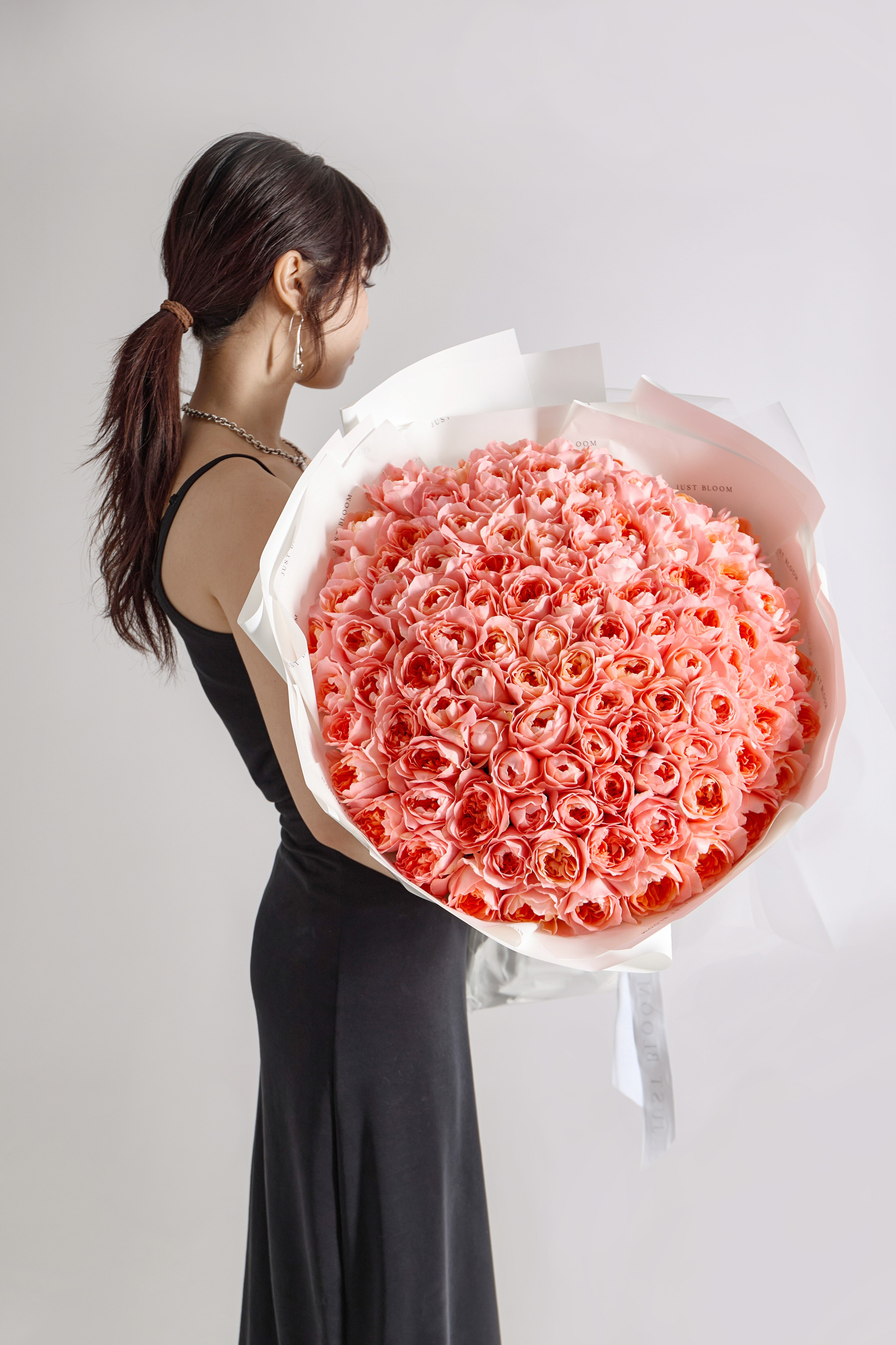 Large luxury bouquet of over 100 pink coral blush roses arranged in dome shape with white and pink wrapping