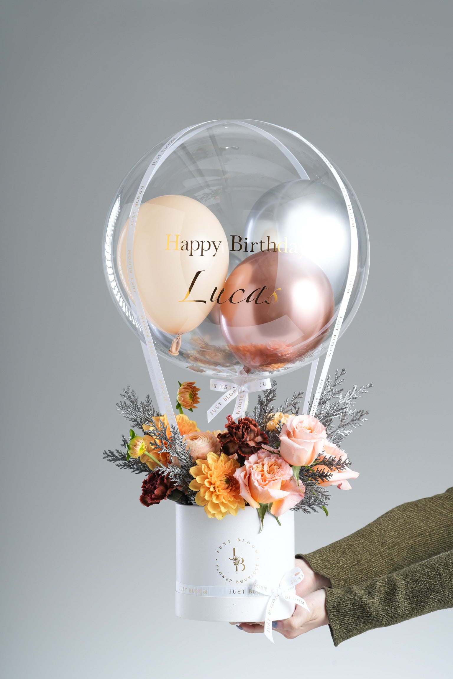 Hand presenting the Briana peach-and-gold balloon flower box against a light-grey background – Just Bloom Hong Kong