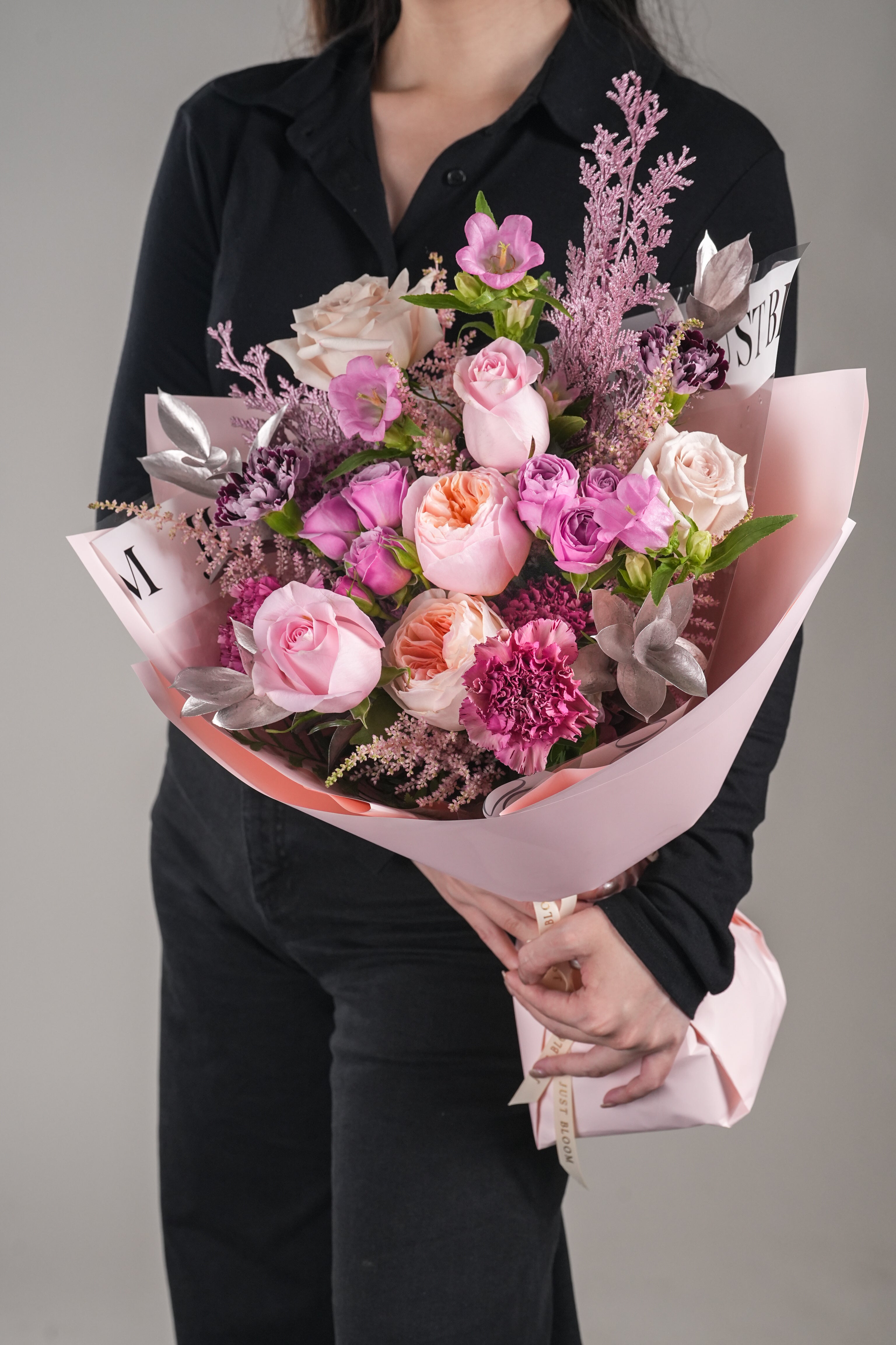 Chelsea romantic Juliet rose bouquet – close-up view of pink and peach garden roses with carnations and filler flowers in pink wrapping.