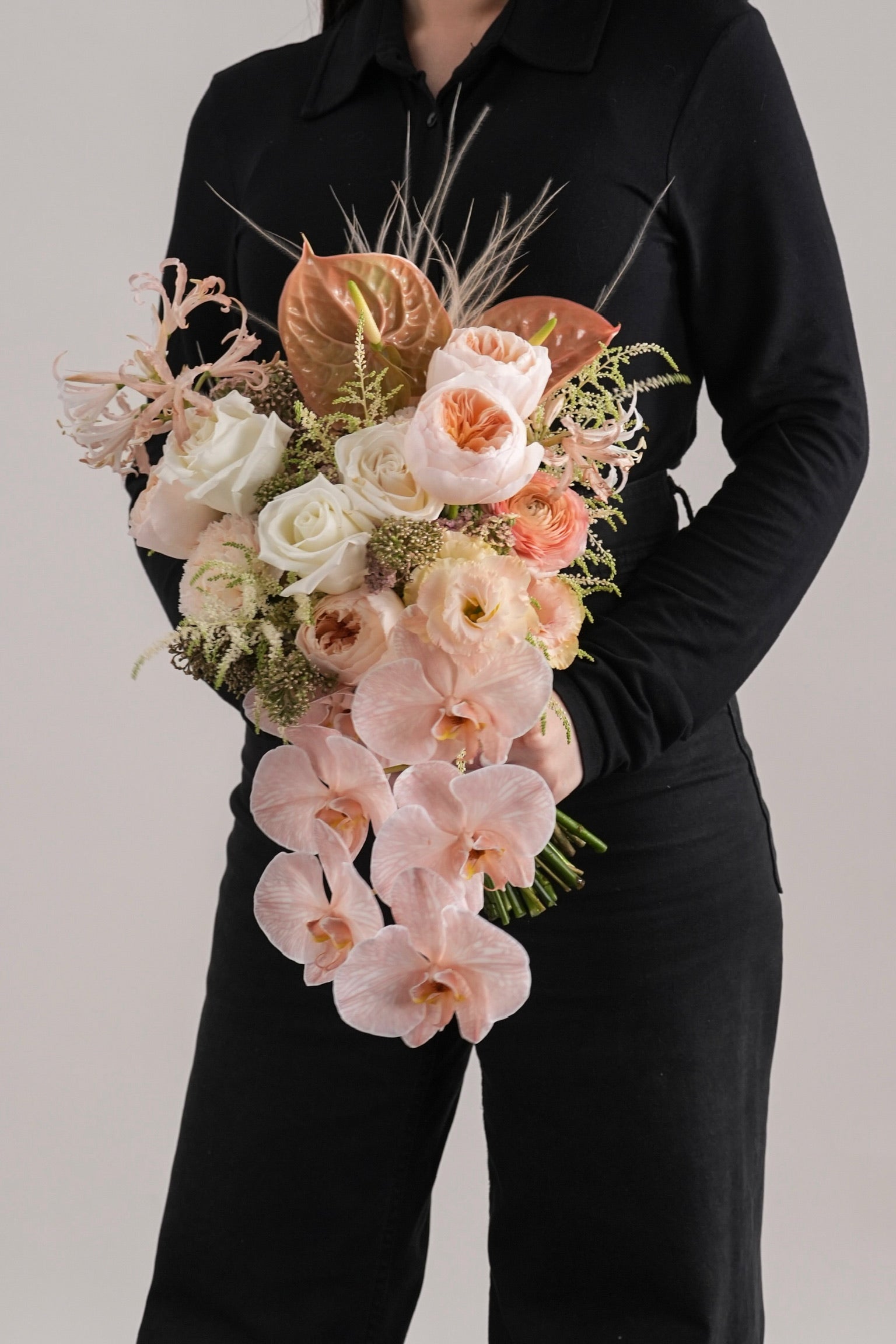 Close-up of Davina peach cascading bouquet held by hands, featuring orchids and roses