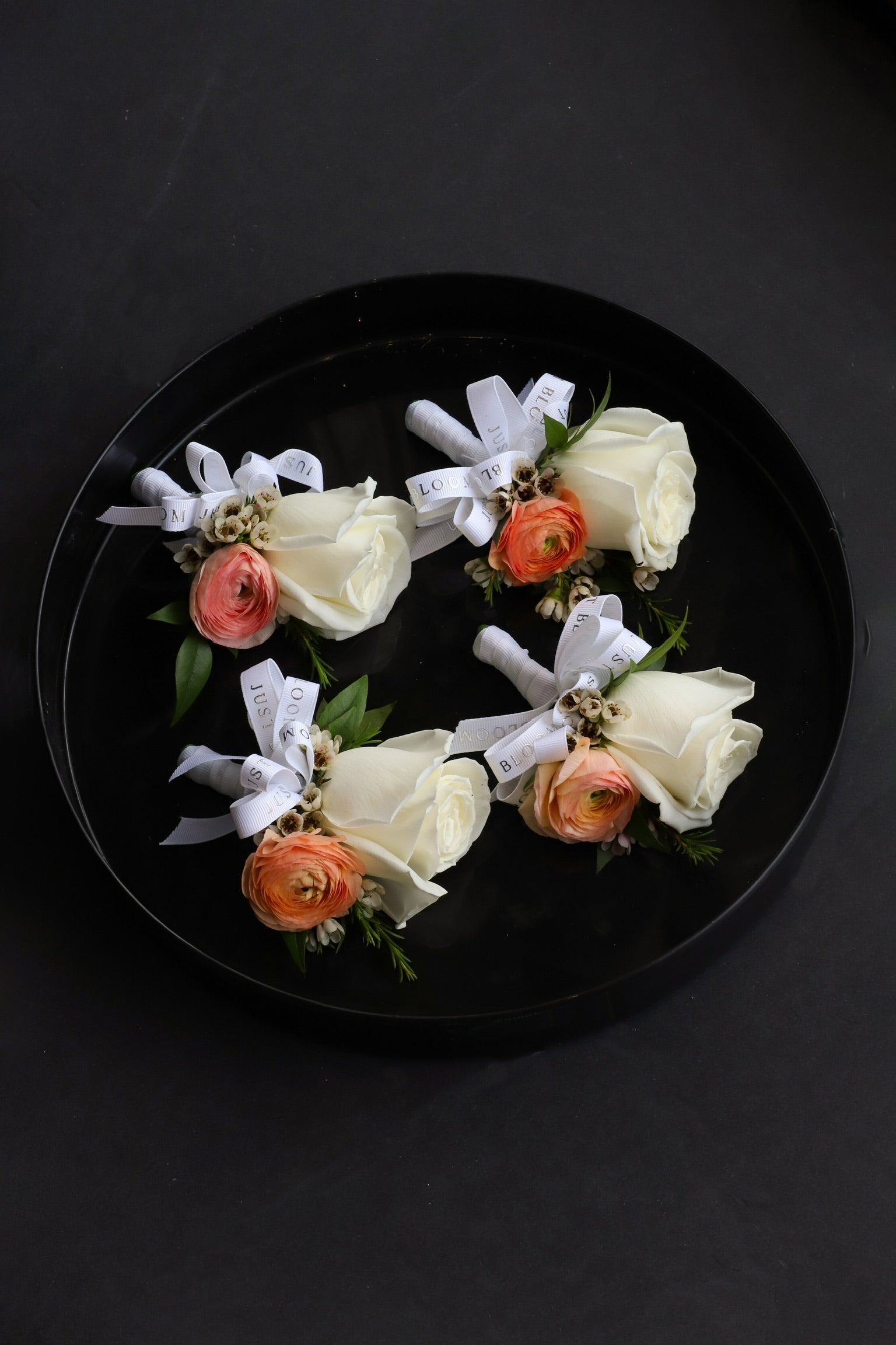 Close-up of four Dear One wedding corsages on a black tray by Just Bloom Hong Kong, showcasing ivory roses, peach ranunculus and wintersweet with fresh foliage