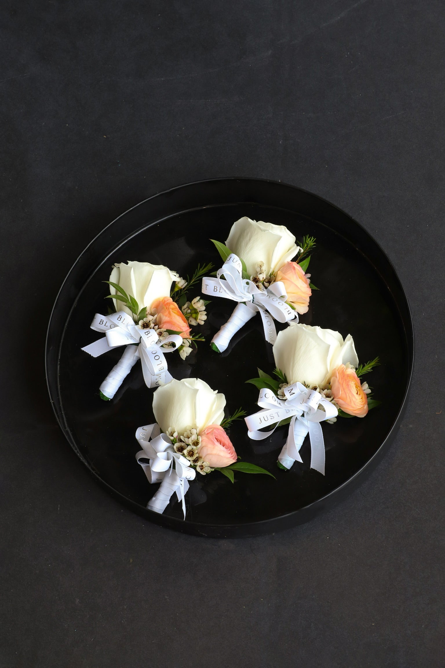 Four Dear One corsages displayed on a black tray by Just Bloom Hong Kong, featuring ivory Ecuadorian roses with soft peach ranunculus, wintersweet and Just Bloom white ribbon