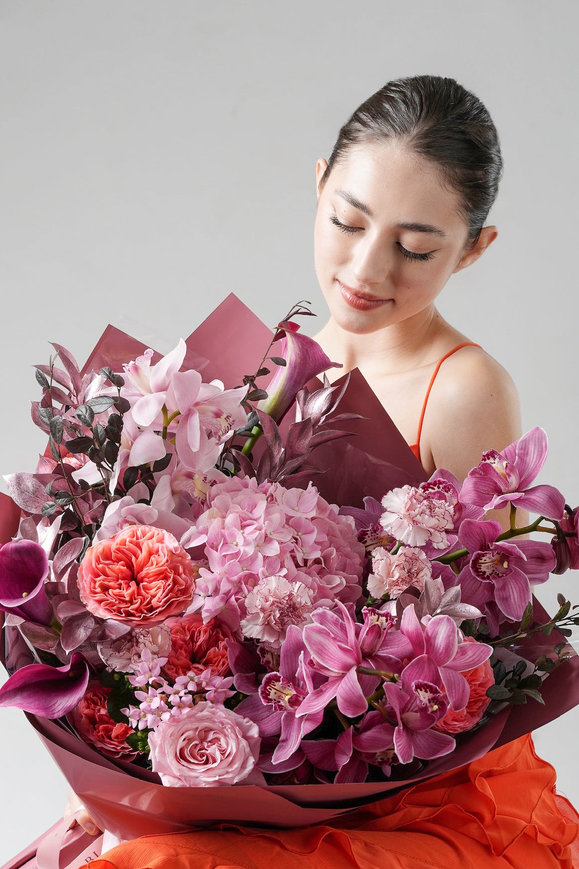 A dramatic bouquet with pink cymbidium orchids, garden roses, and metallic foliage in soft blush and deep coral tones.