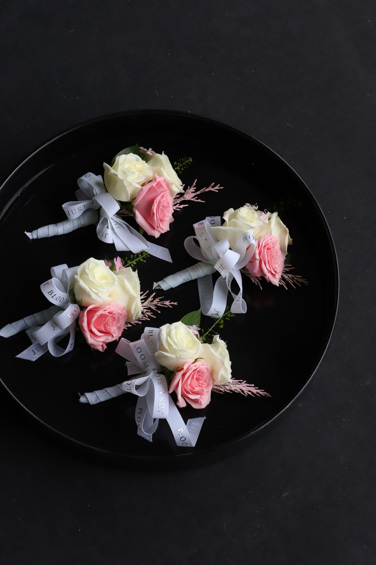 Close-up of four Endless Love wedding corsages on a black tray by Just Bloom Hong Kong, showcasing white and pink Ecuadorian roses with frosted explosion, astilbes and Just Bloom white ribbon