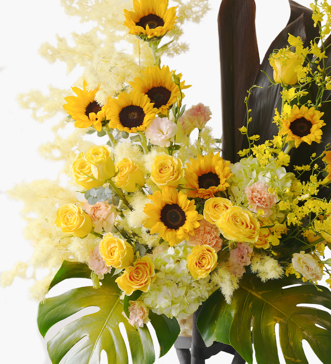 Close-up of Evangeline flower stand – sunflowers and mixed blooms with tropical leaves for grand event setup