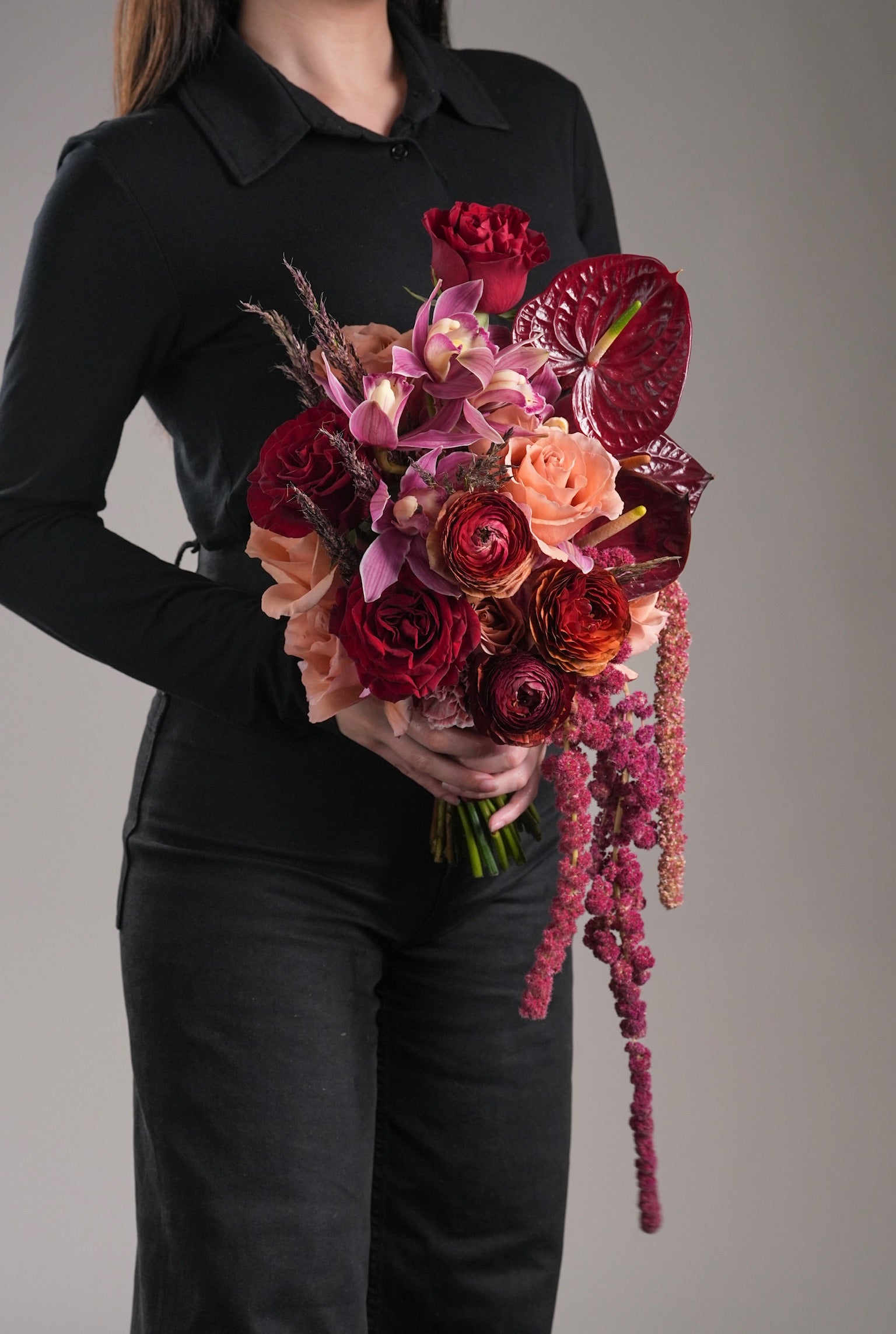 holding cascading bridal bouquet with pink orchids and roses in soft focus