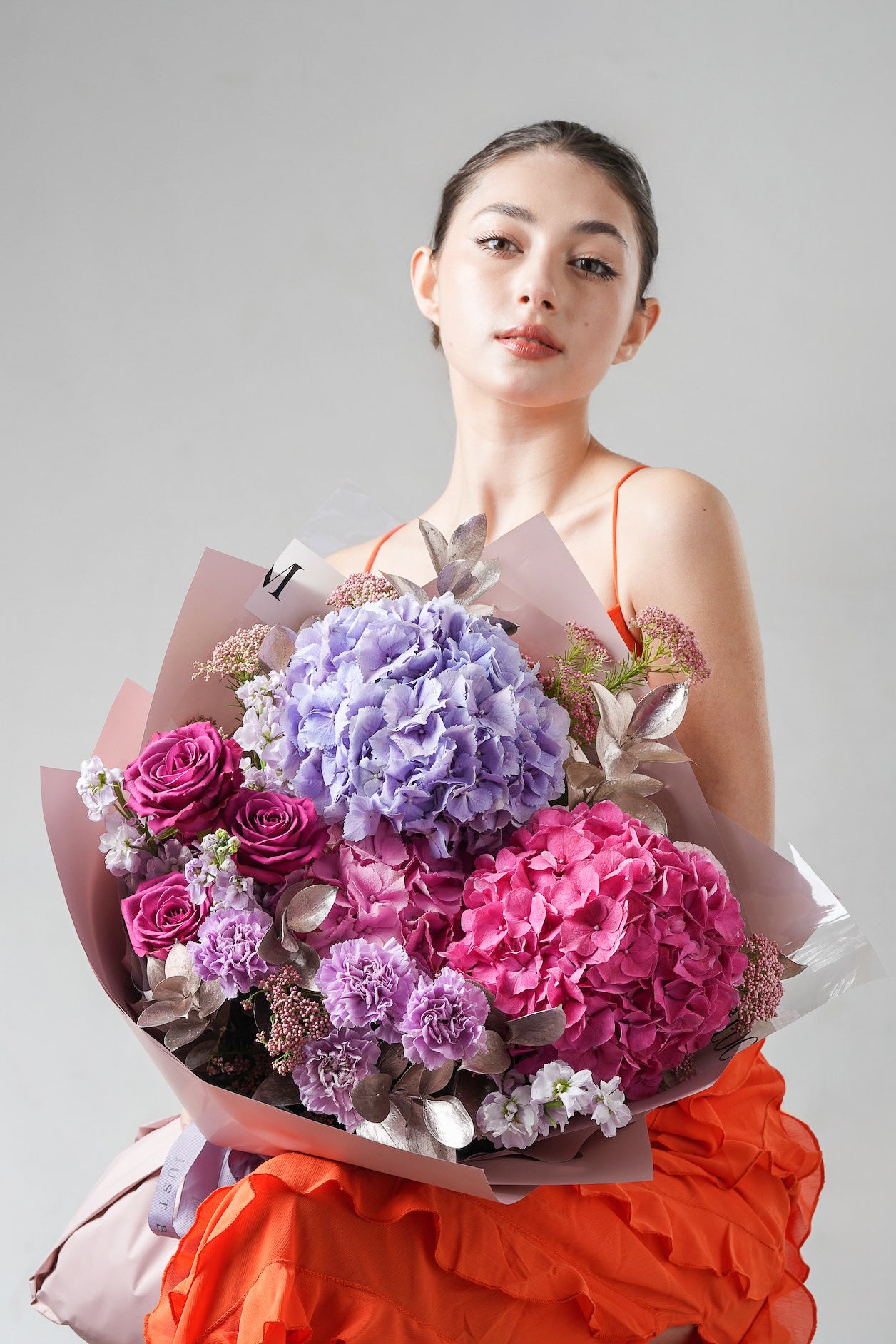 Refined floral arrangement in soft purple and pink tones, accented with metallic foliage.