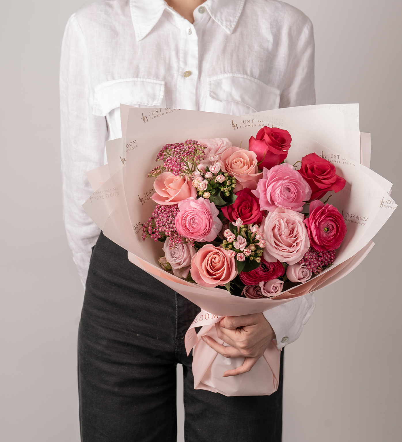 Woman in white shirt holding Camryn pink rose and ranunculus bouquet wrapped in blush paper.