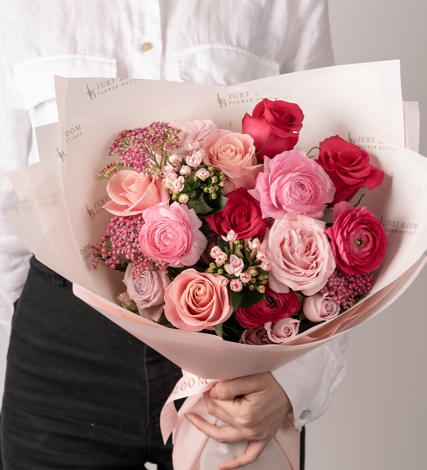 Close-up of Camryn bouquet showing Ecuadorian roses, ranunculus, and wax flowers in pink tones.
