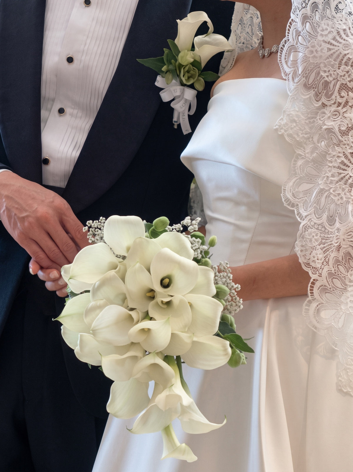 Real wedding photo of A Lifetime with You bridal bouquet held by a bride in a white lace gown, paired with a matching boutonnière on the groom's tuxedo lapel
