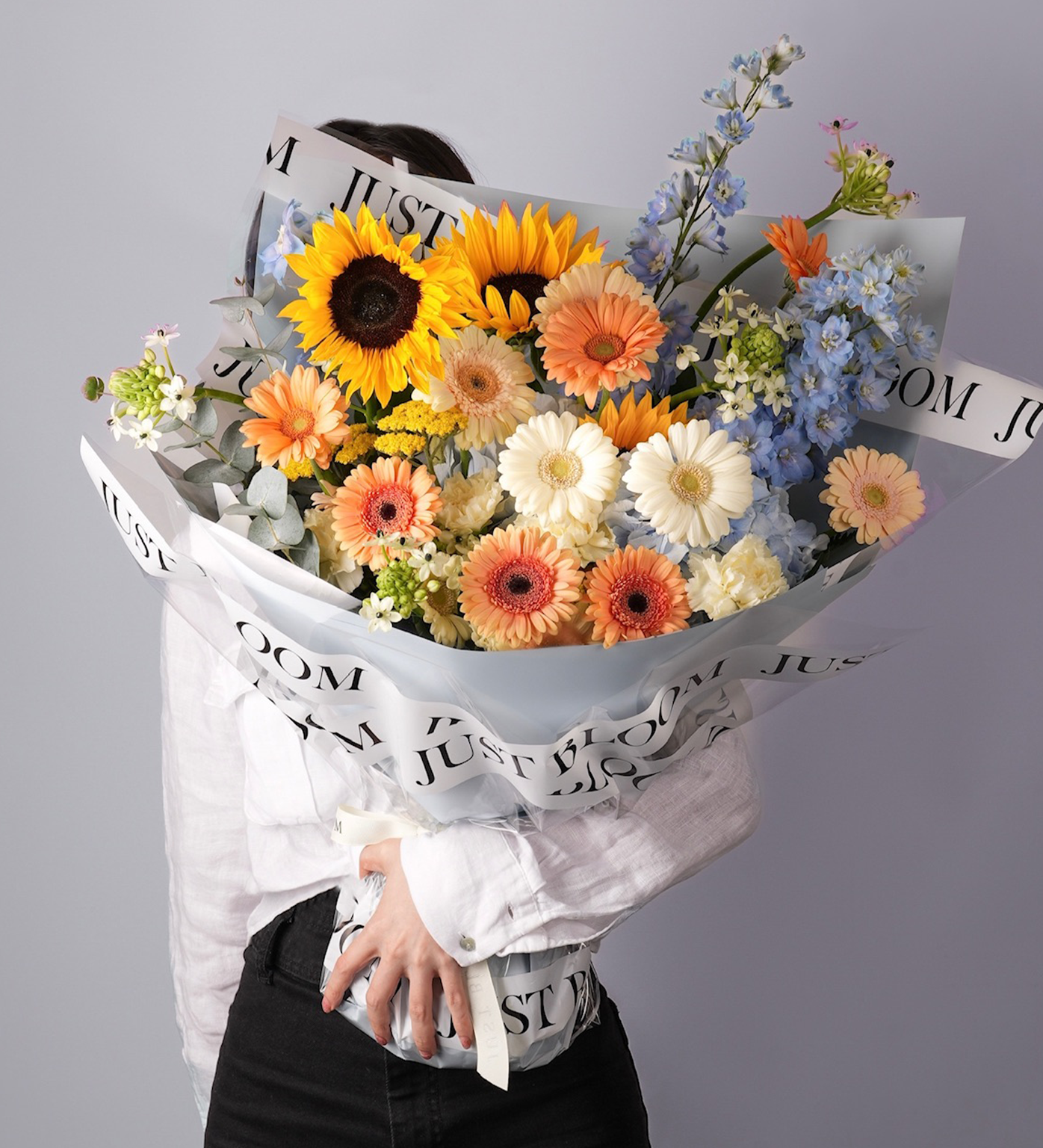 Large sunflower and gerbera flower bouquet with orange, yellow, and pastel blue Dutch blooms, wrapped in white Just Bloom Hong Kong packaging – perfect for birthdays or congratulations.