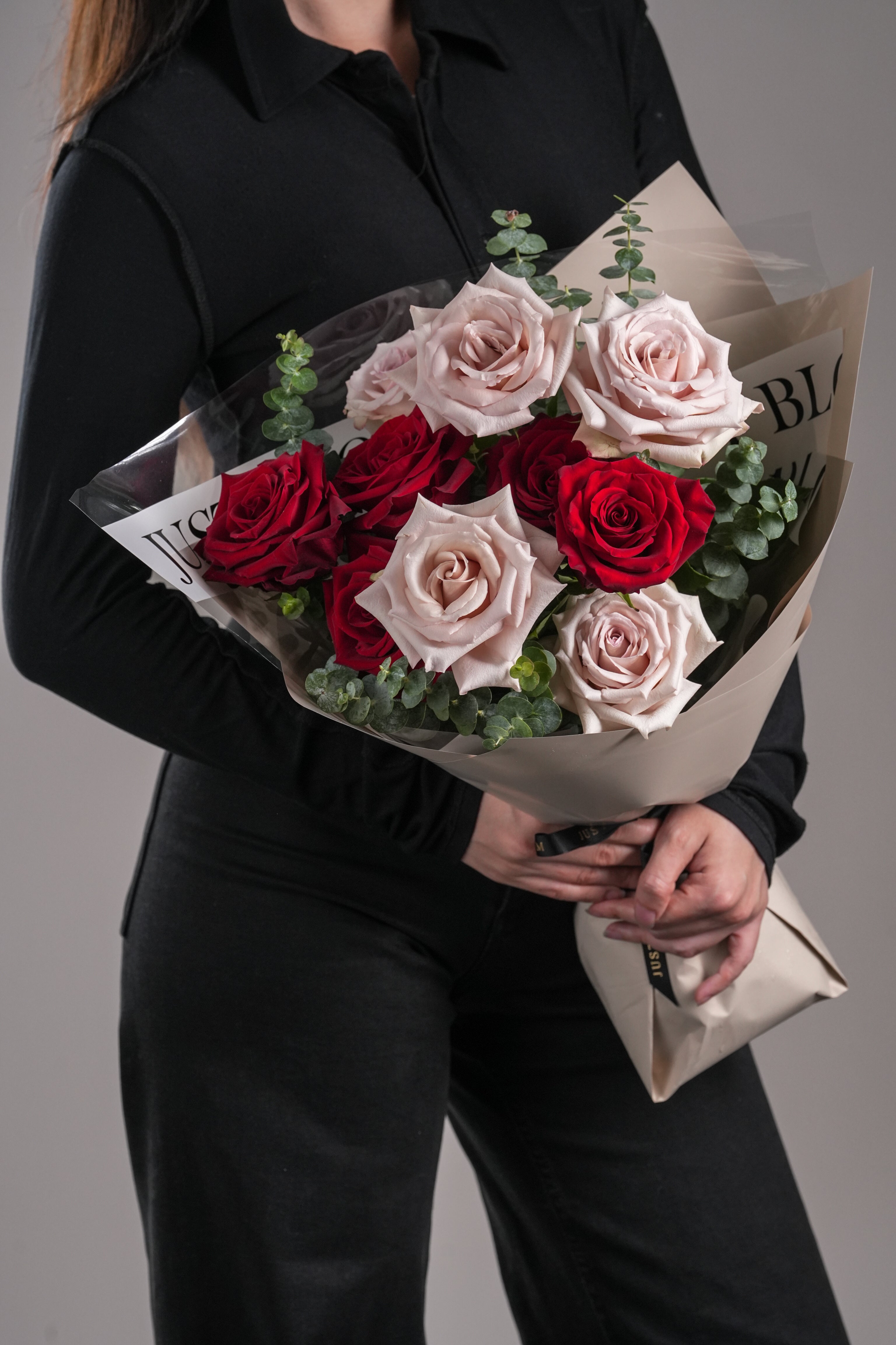 Ares bouquet of red and quicksand roses with eucalyptus, held in front of a black outfit