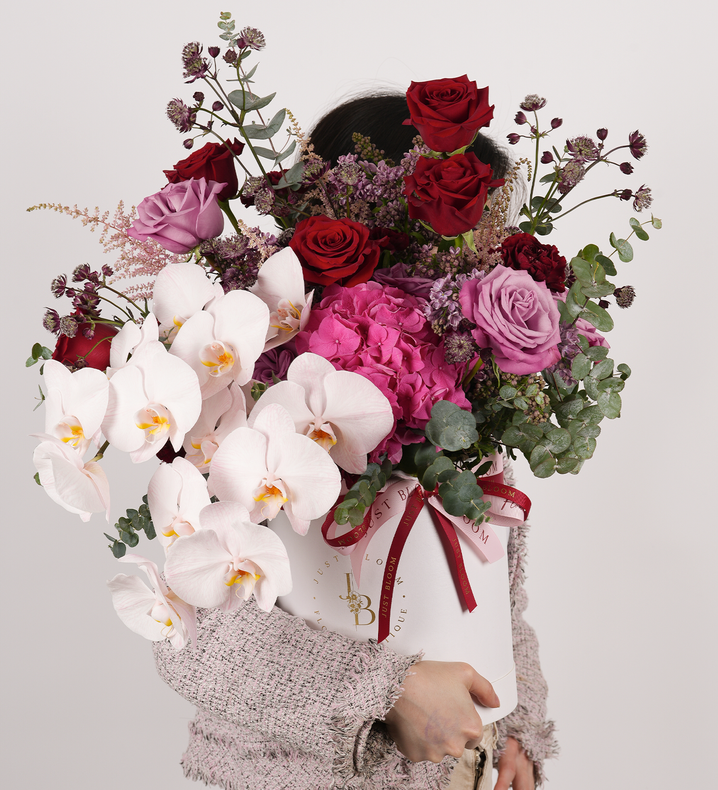 Michelle being held, showcasing orchids, roses, hydrangeas, and eucalyptus in purple, pink, and red