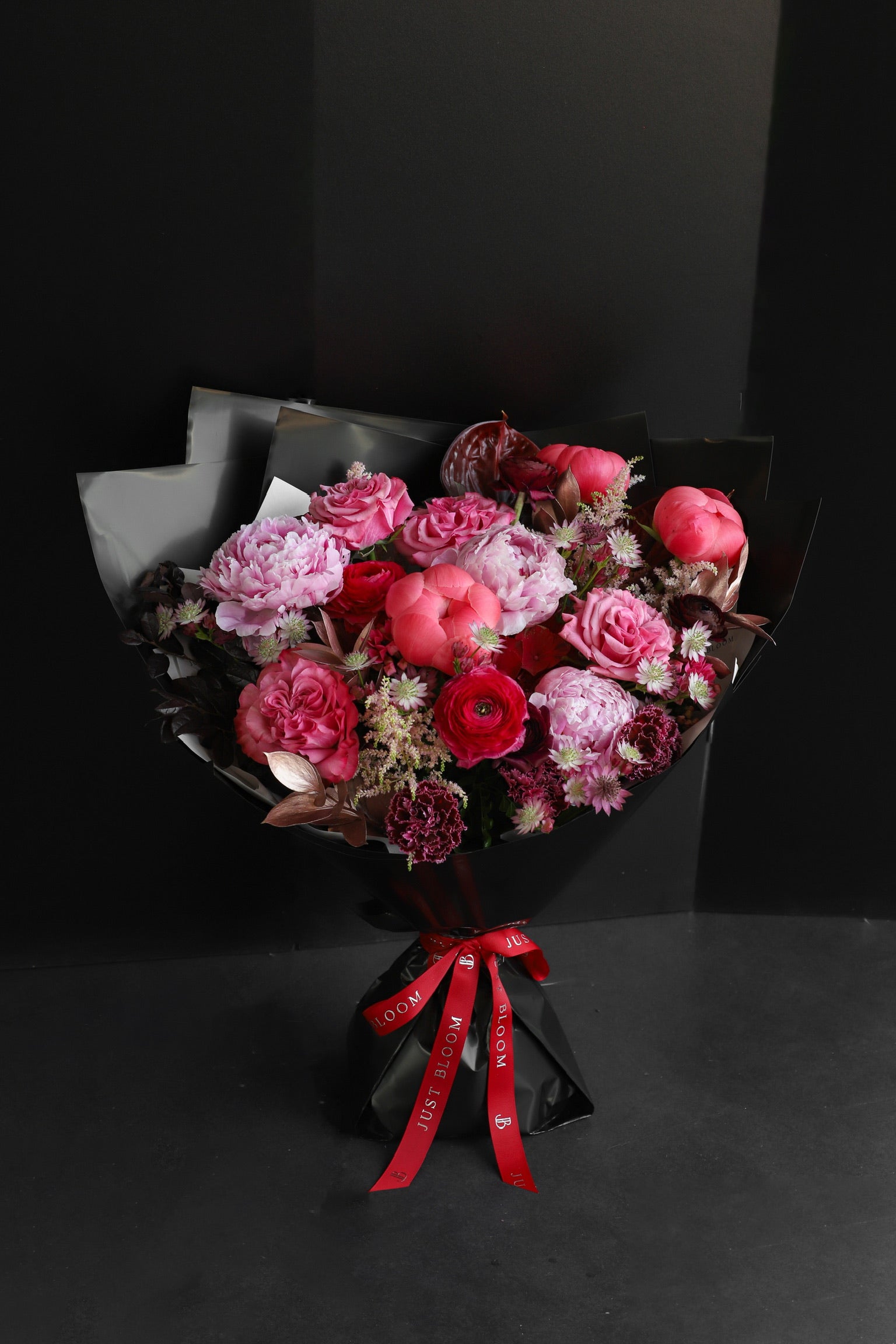Midnight Peonies luxury bouquet by Just Bloom Hong Kong featuring peonies, ranunculus, roses, astilbes, carnations, anthuriums and astrantias wrapped in black with a Just Bloom red ribbon