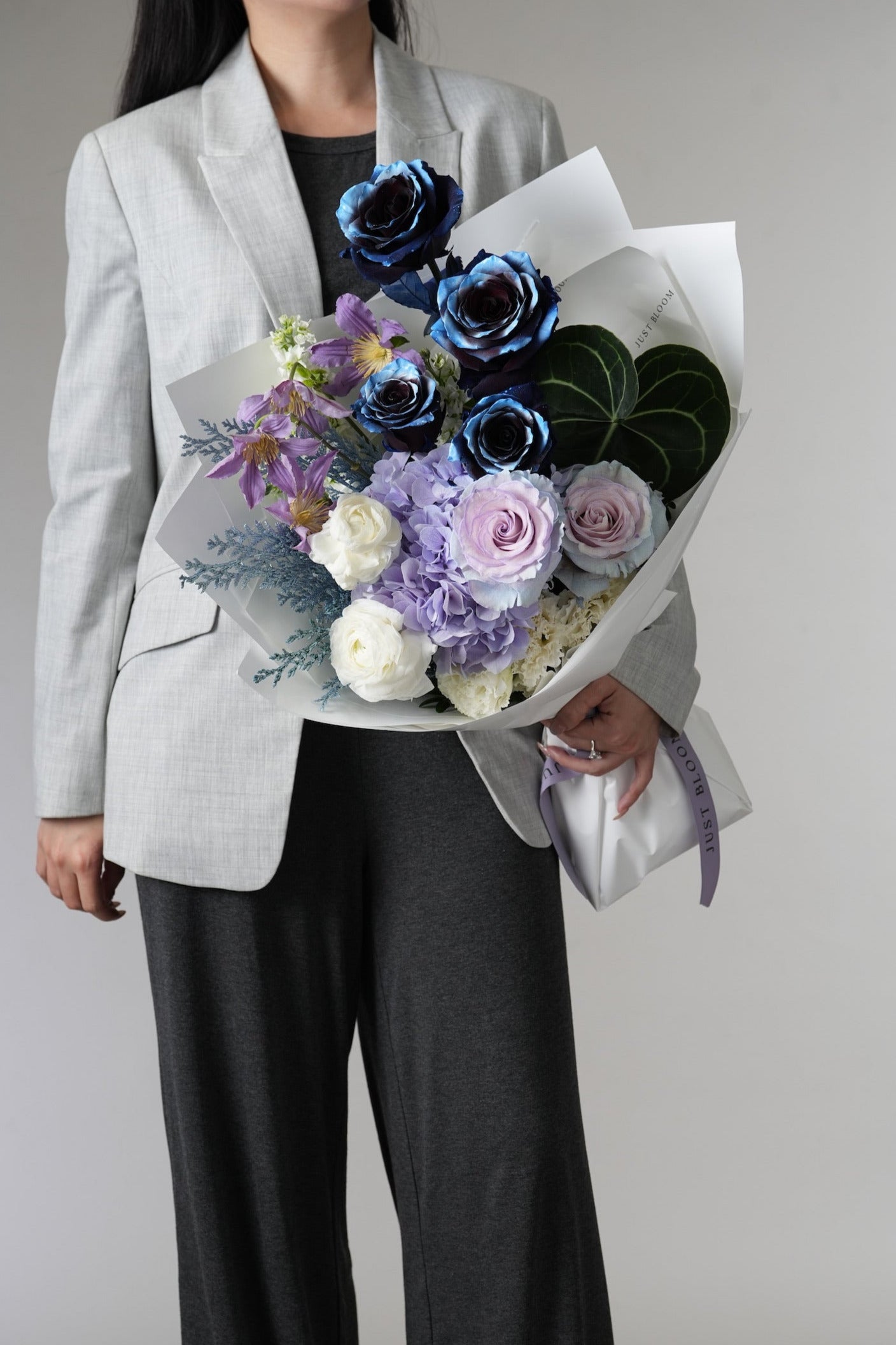 Noctis floral arrangement with purple clematis and elegant wrapping held by model