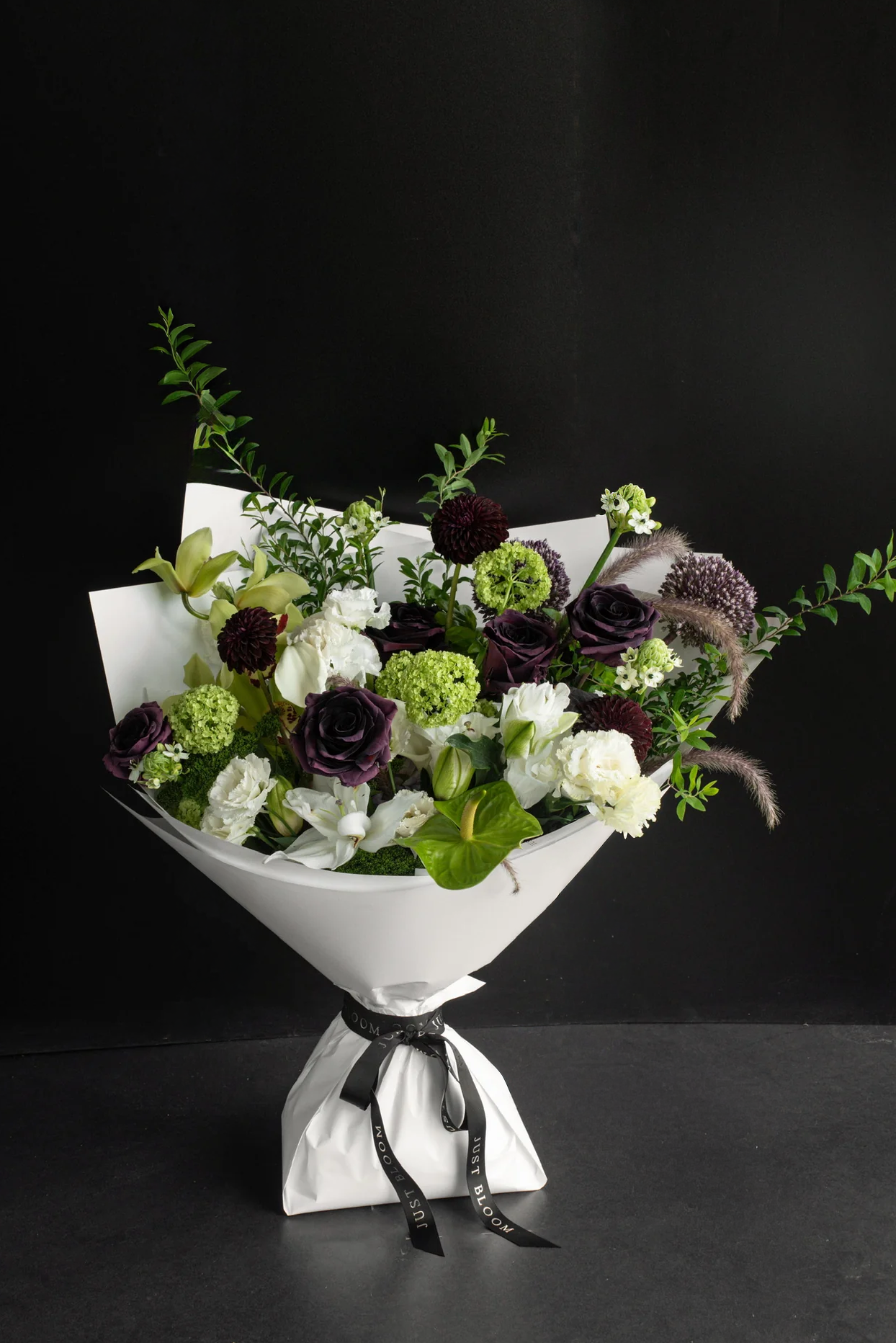 Large dark-toned fresh flower bouquet in deep plum, lime green, and white with mixed seasonal blooms and greenery wrapped in white Just Bloom paper against a dark background — Just Bloom Hong Kong