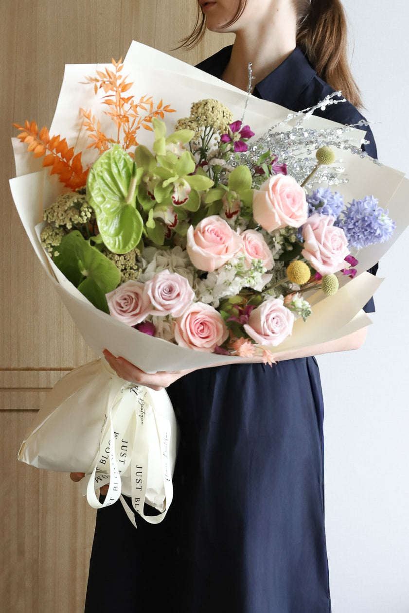 A model holding One & Only luxury bouquet by Just Bloom Hong Kong, showcasing an unexpected mix of blush roses, lavender blooms, green anthuriums and shimmering silver stems in ivory wrapping