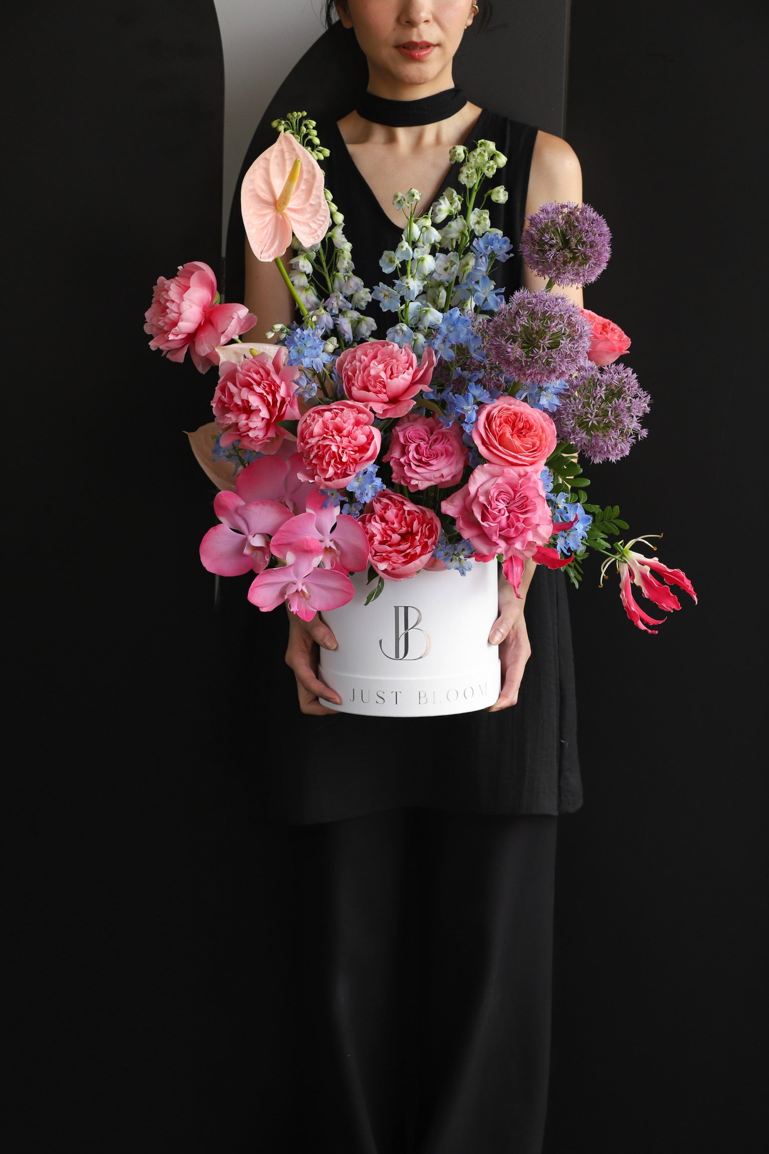 Model holding a vibrant large flower box arrangement in hot pink and purple tones with mixed seasonal blooms in a white Just Bloom hat box against a dark background — Just Bloom Hong Kong