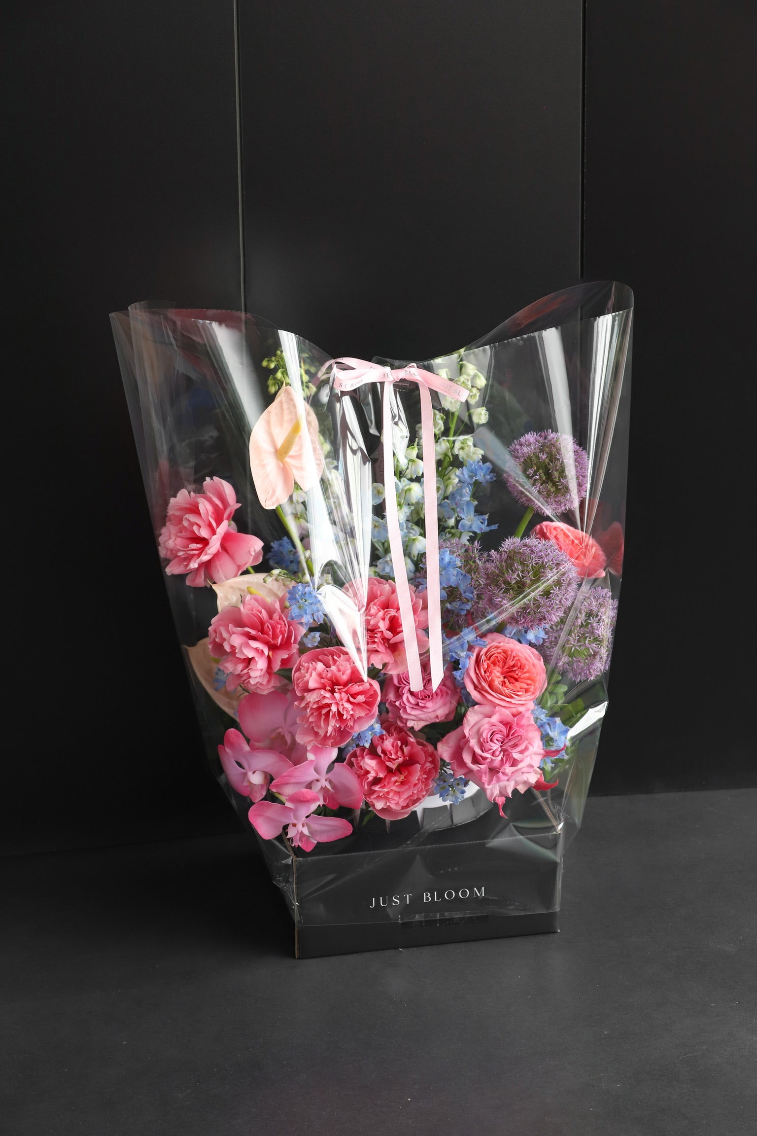 Just Bloom flower box arrangement in clear gift packaging with pink ribbon, showing vibrant pink and purple blooms against a dark background — Just Bloom Hong Kong