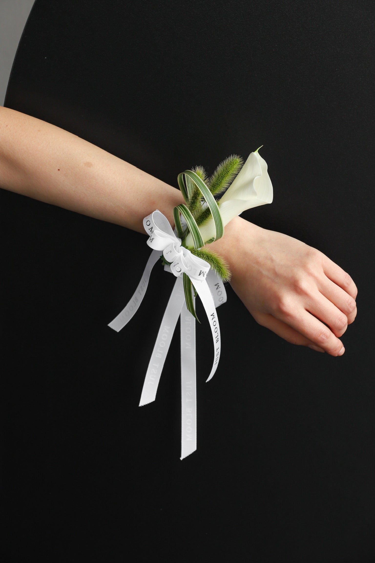 A model wearing the Pure Intention wrist corsage featuring a white calla lily, spider plant and foxtail grass tied with a Just Bloom white ribbon — Just Bloom Hong Kong