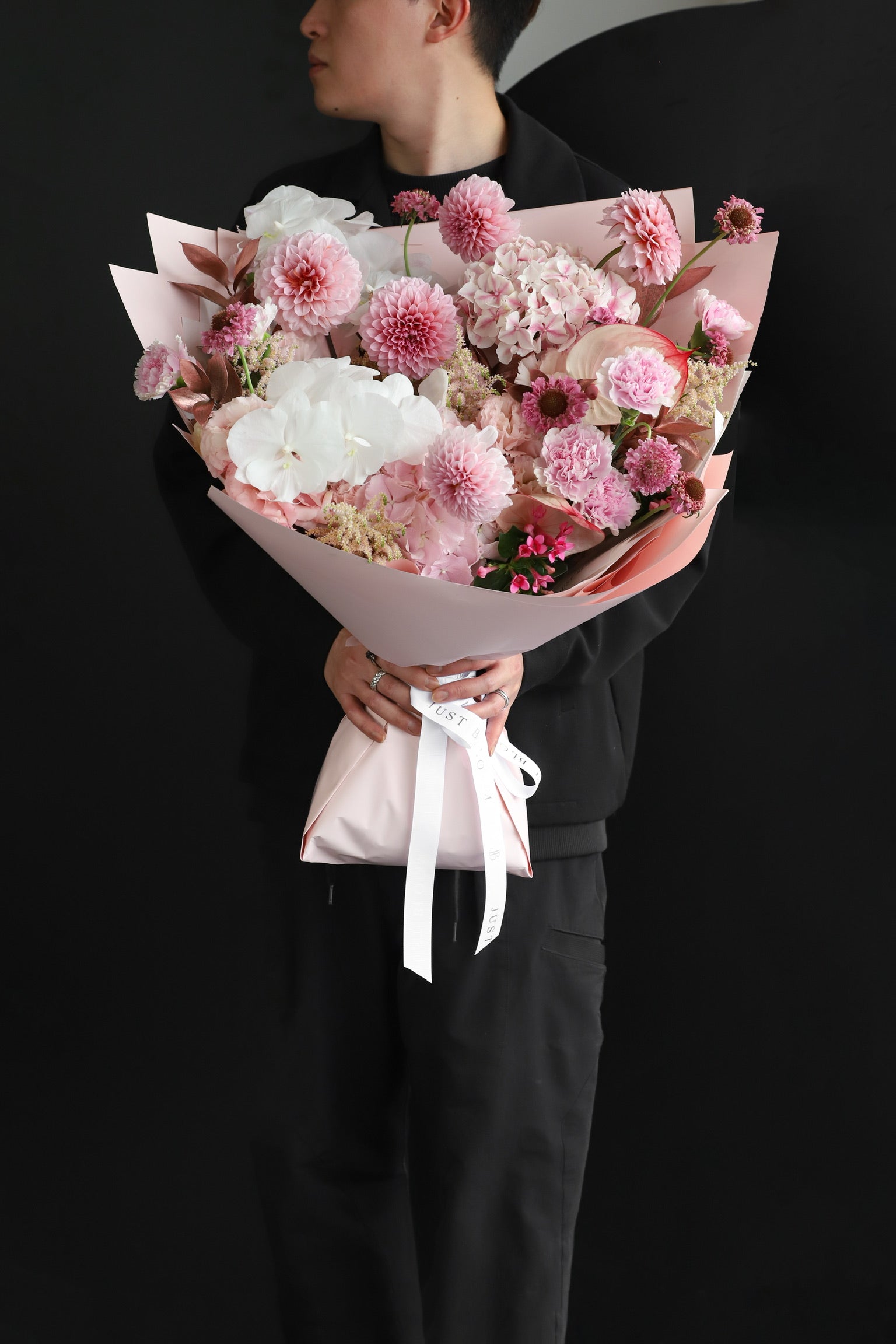 Model holding an oversized soft pink and white fresh flower bouquet with layered blooms of varying textures wrapped in blush pink Just Bloom paper — Just Bloom Hong Kong