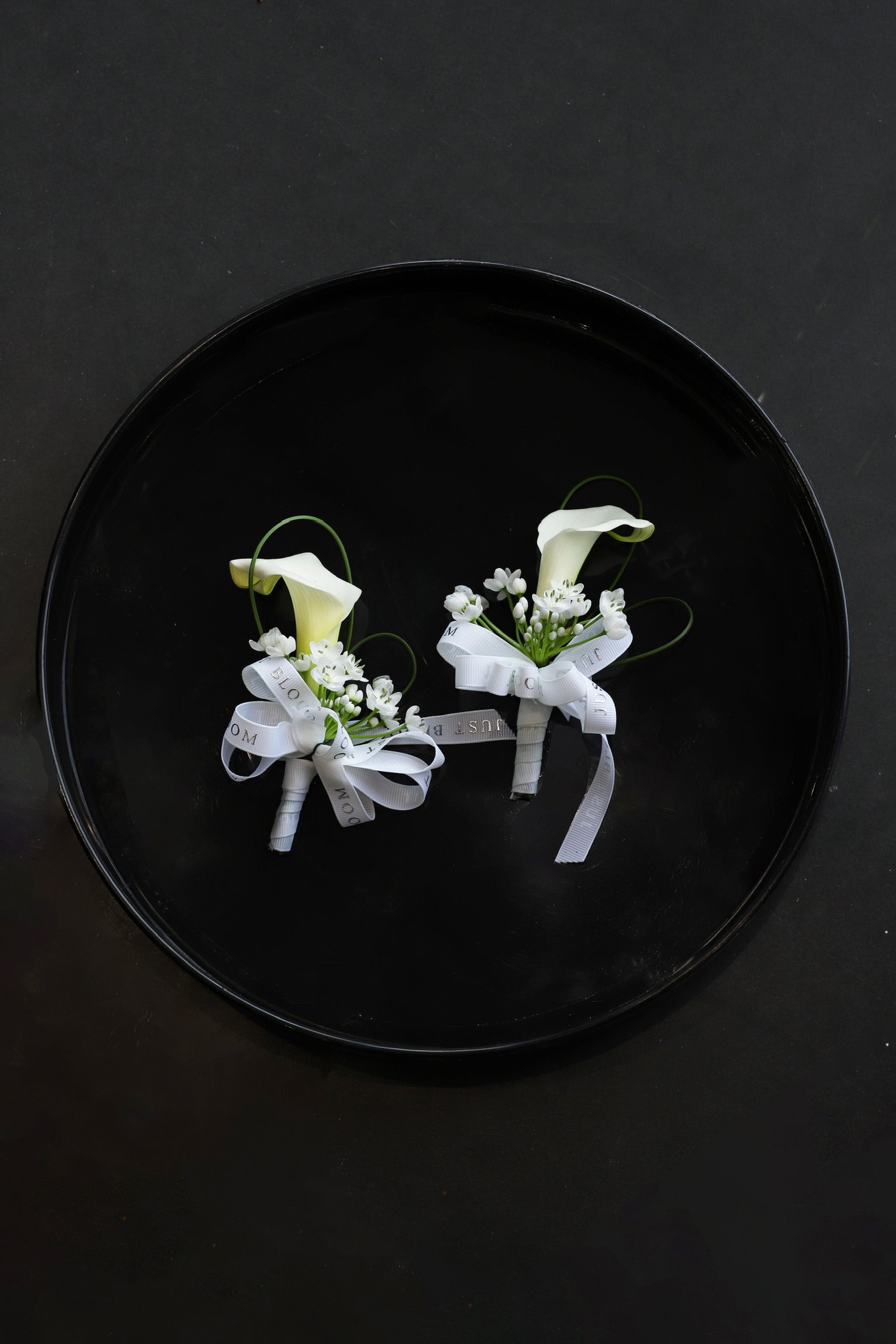 Two Simply White corsages arranged on a black tray featuring white calla lilies, allium cowanii and spiral steel grass tied with Just Bloom white ribbon — Just Bloom Hong Kong