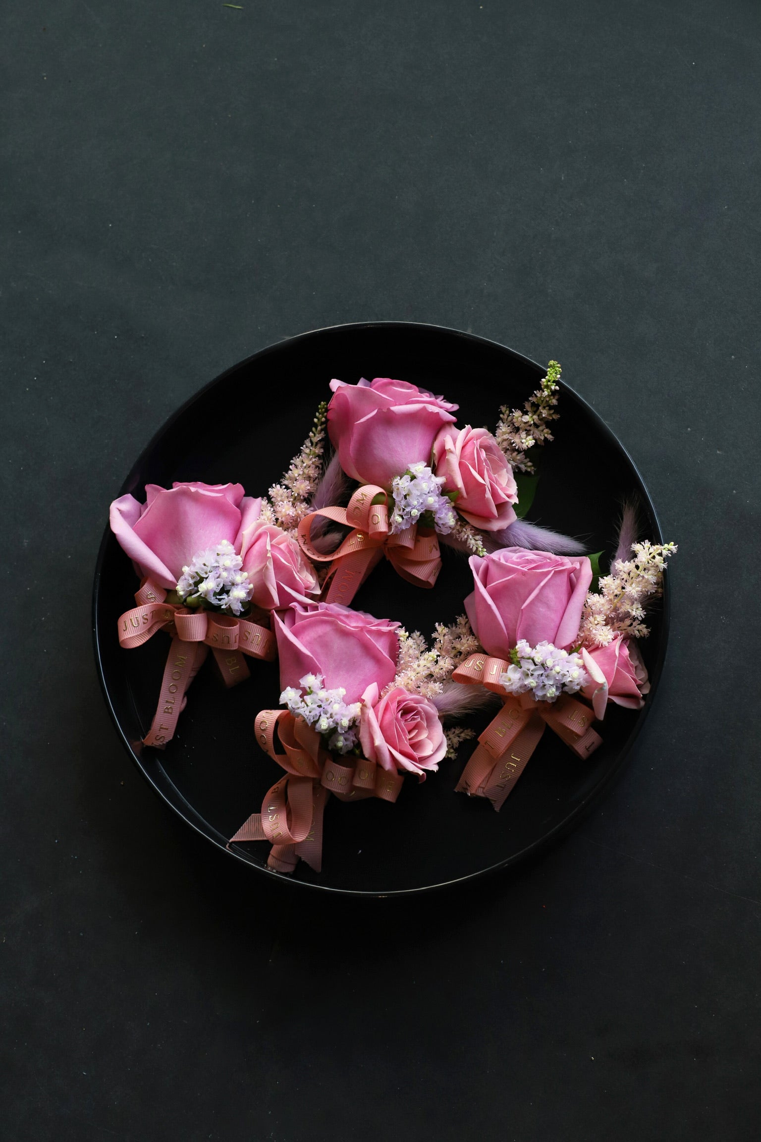 Four Boutonnieres arranged on a black tray featuring pink Ecuadorian roses, spray roses, pink astilbes and myosotis tied with Just Bloom rose gold ribbon — Just Bloom Hong Kong