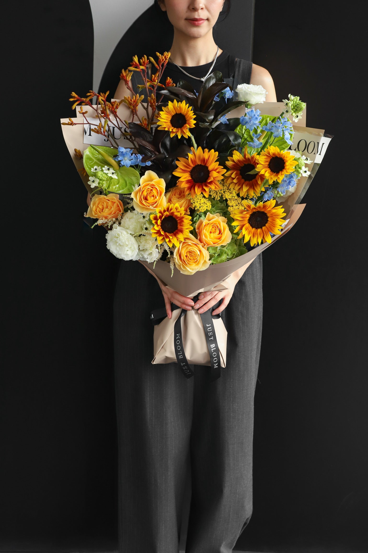 Model holding an oversized fresh flower bouquet with Japanese sunflowers, roses, and mixed blooms in warm amber and blue tones, wrapped in Just Bloom kraft paper — Just Bloom Hong Kong