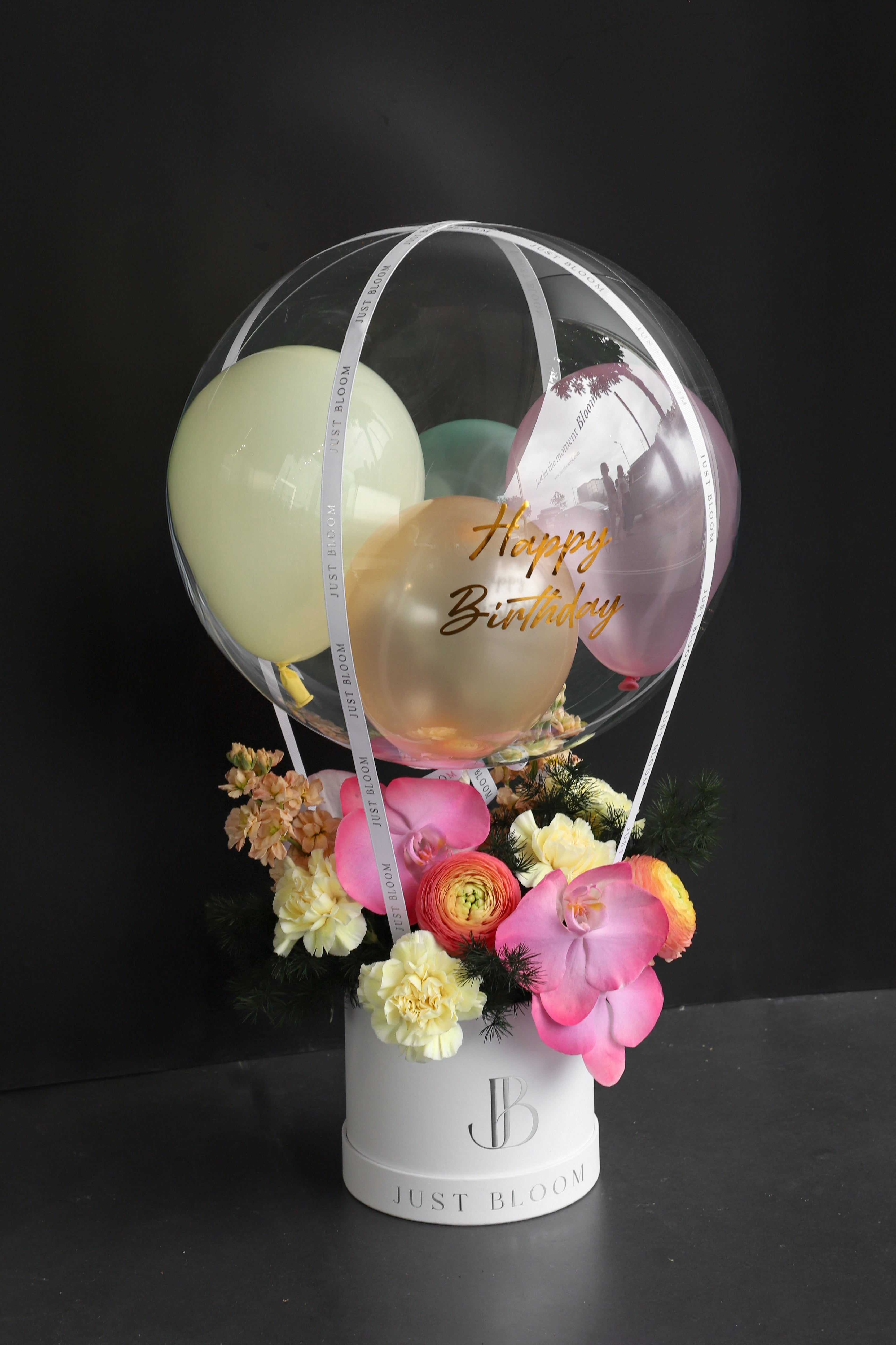 Fresh flower box with pink Phalaenopsis Orchids, orange Ranunculus, cream Carnations, and dark greenery in a white Just Bloom round box against a dark background — Just Bloom Hong Kong