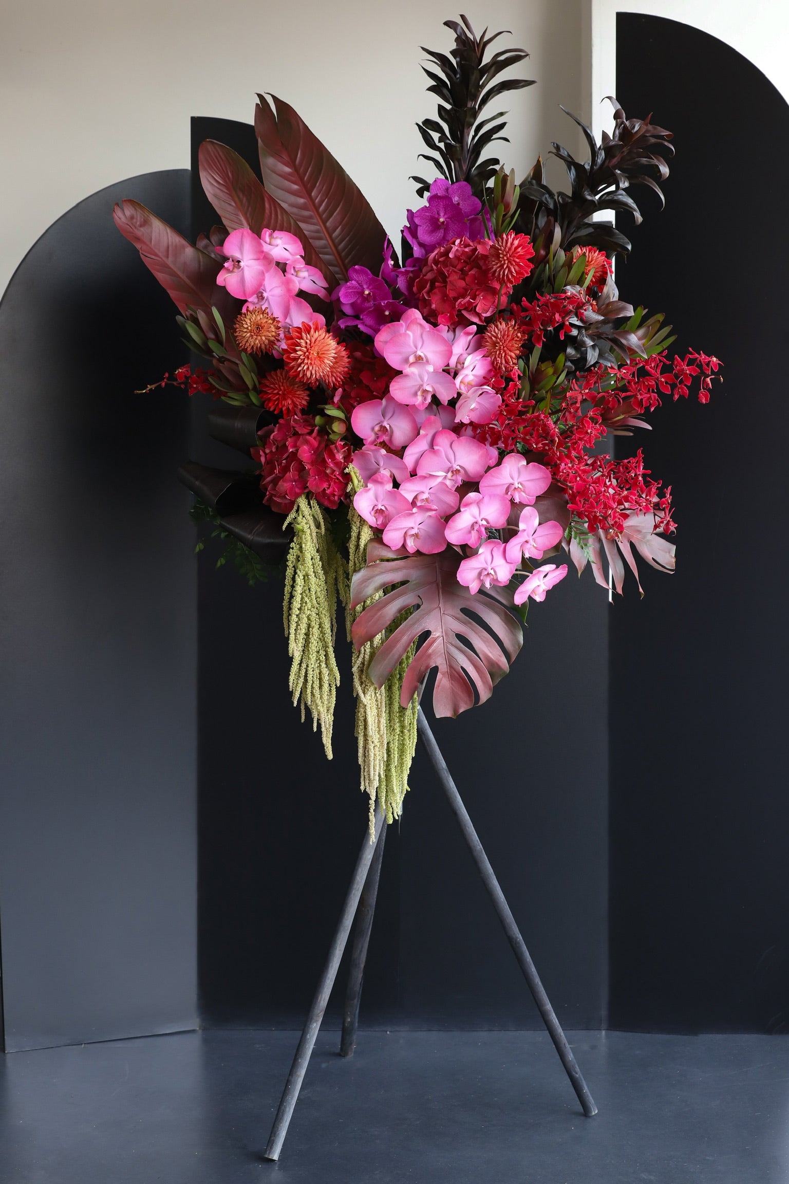 A dramatic luxury flower stand featuring deep red, fuchsia and magenta blooms with dark tropical foliage and cascading lime green tendrils — Tropical Fire by Just Bloom Hong Kong