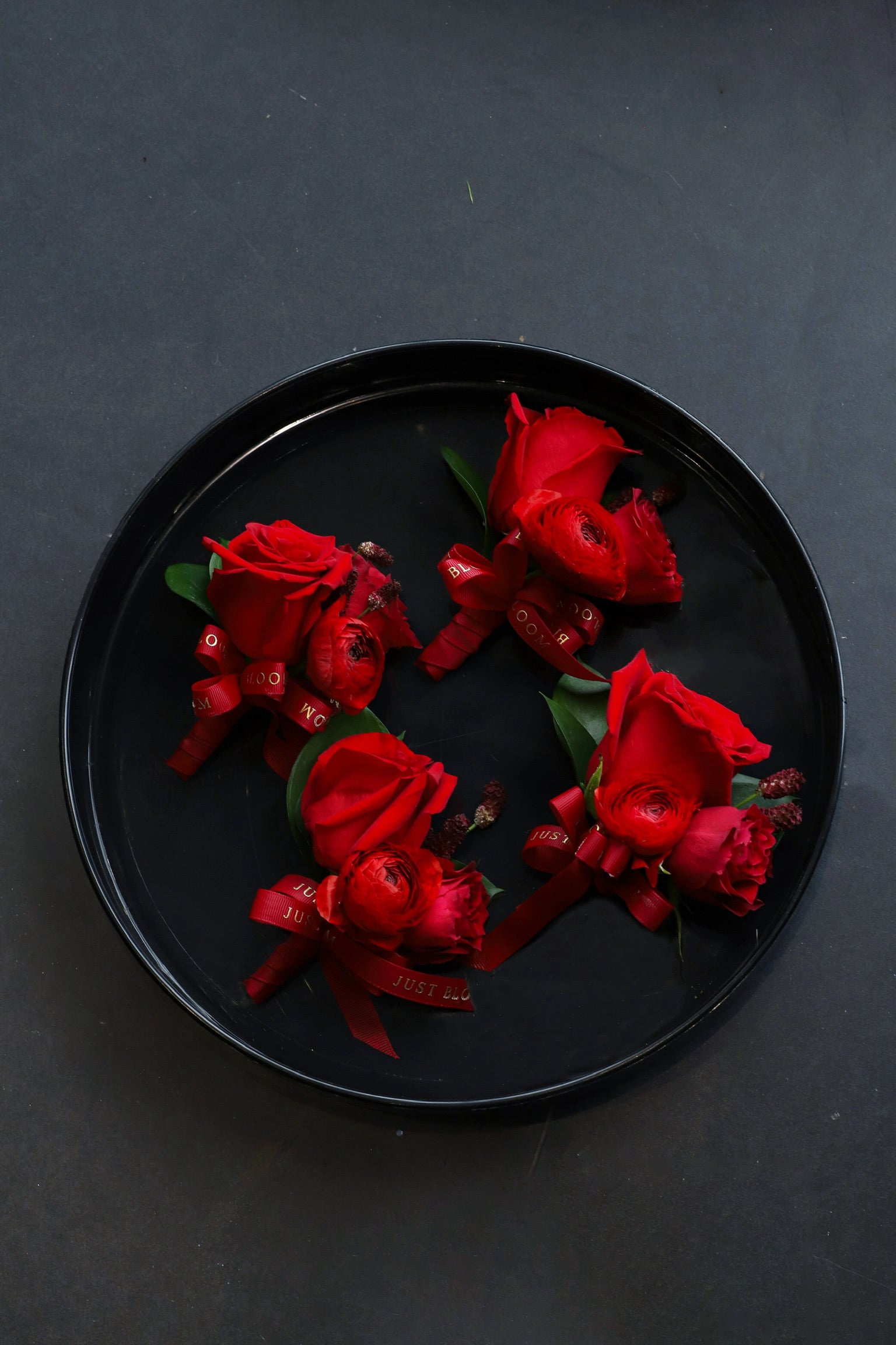 Four True Red corsages arranged on a black tray featuring deep red Ecuadorian roses, spray roses, ranunculus and seasonal berries tied with Just Bloom deep red ribbon — Just Bloom Hong Kong