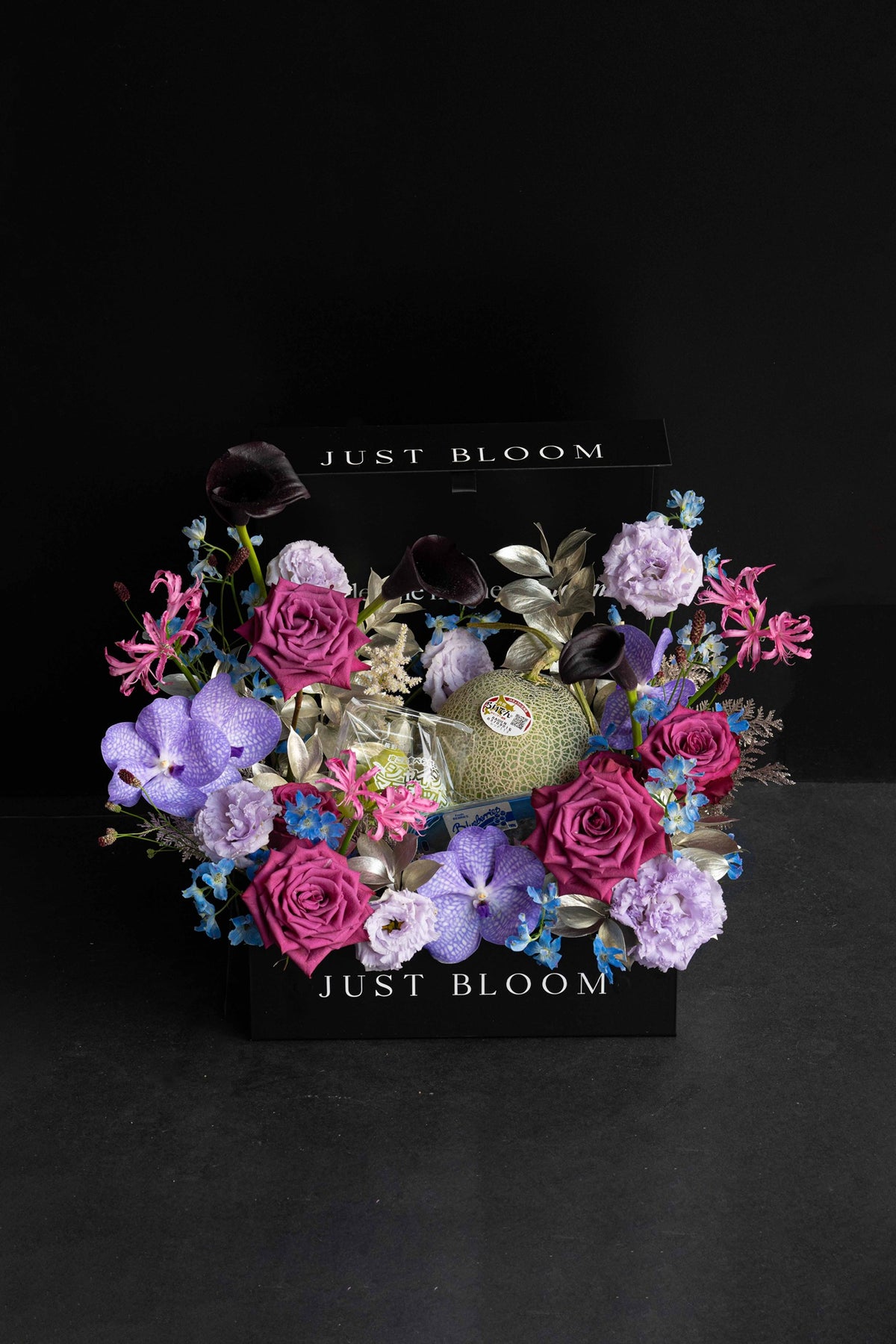 Large purple and magenta luxury floral hamper with a Japanese Melon, Shine Muscat grapes, and blueberries in a black Just Bloom box against a dark background — Just Bloom Hong Kong