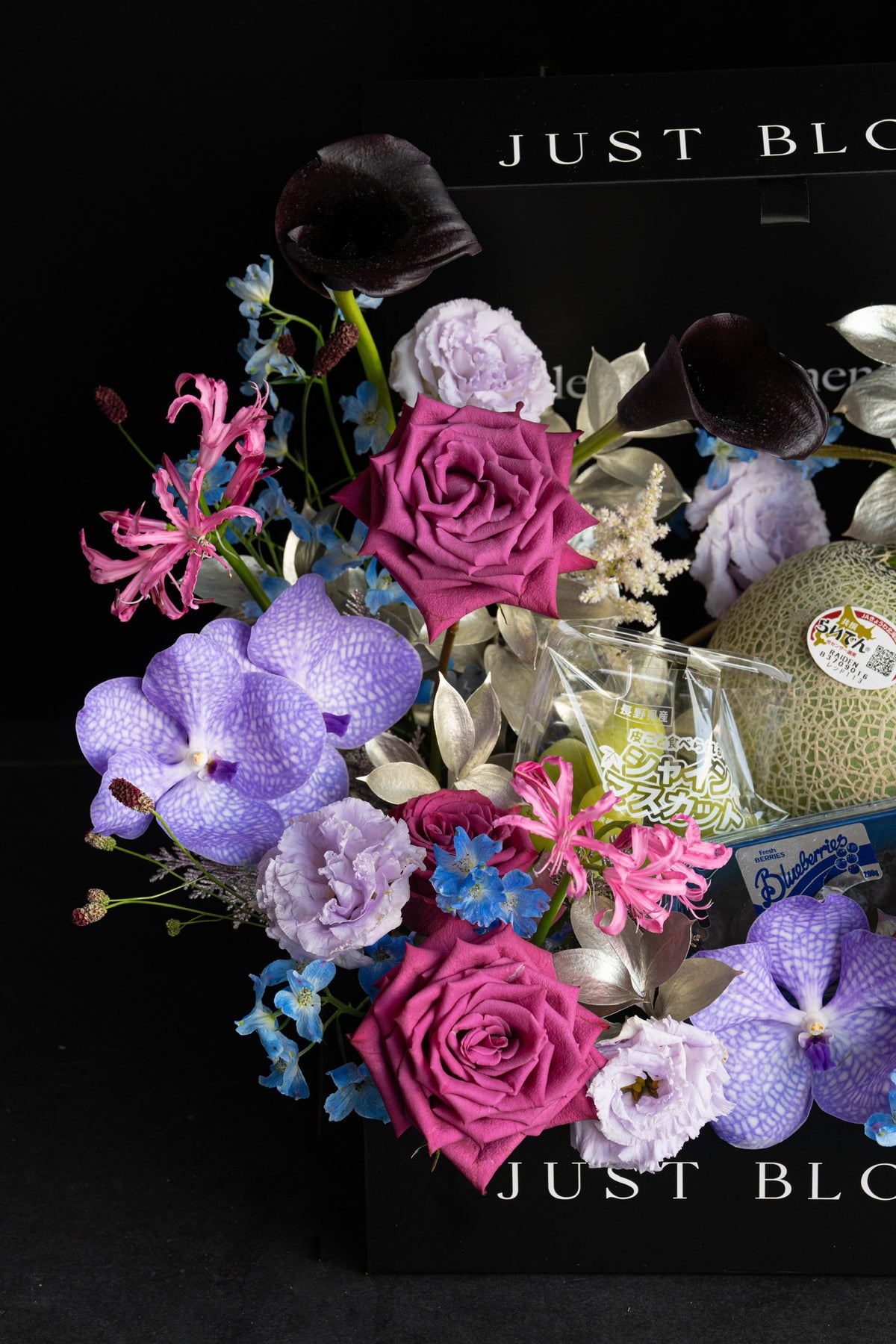 Close-up of a luxury floral hamper in deep purple and magenta with premium Japanese Melon, Shine Muscat grapes, and blueberries nestled within the floral arrangement — Just Bloom Hong Kong