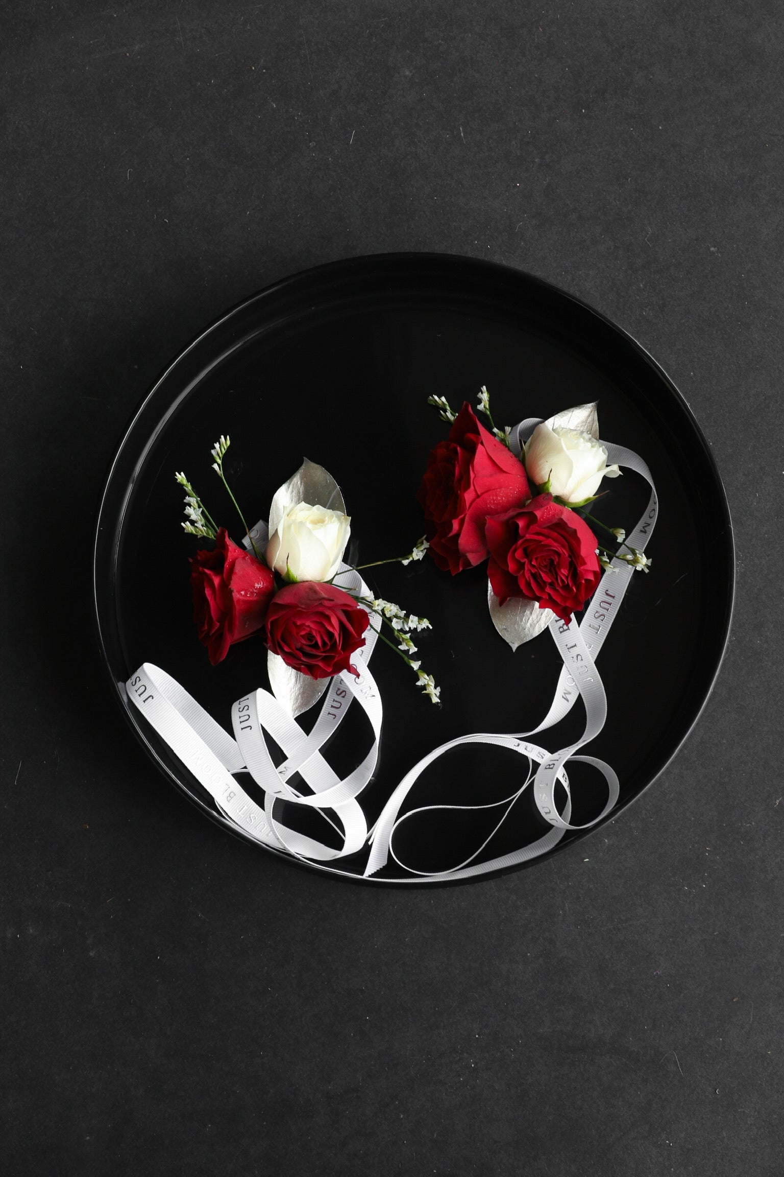 Two Wrist Corsage No.4 pieces arranged on a black tray featuring deep red roses, a white rose, seasonal fillers and silver foliage with Just Bloom white ribbon — Just Bloom Hong Kong