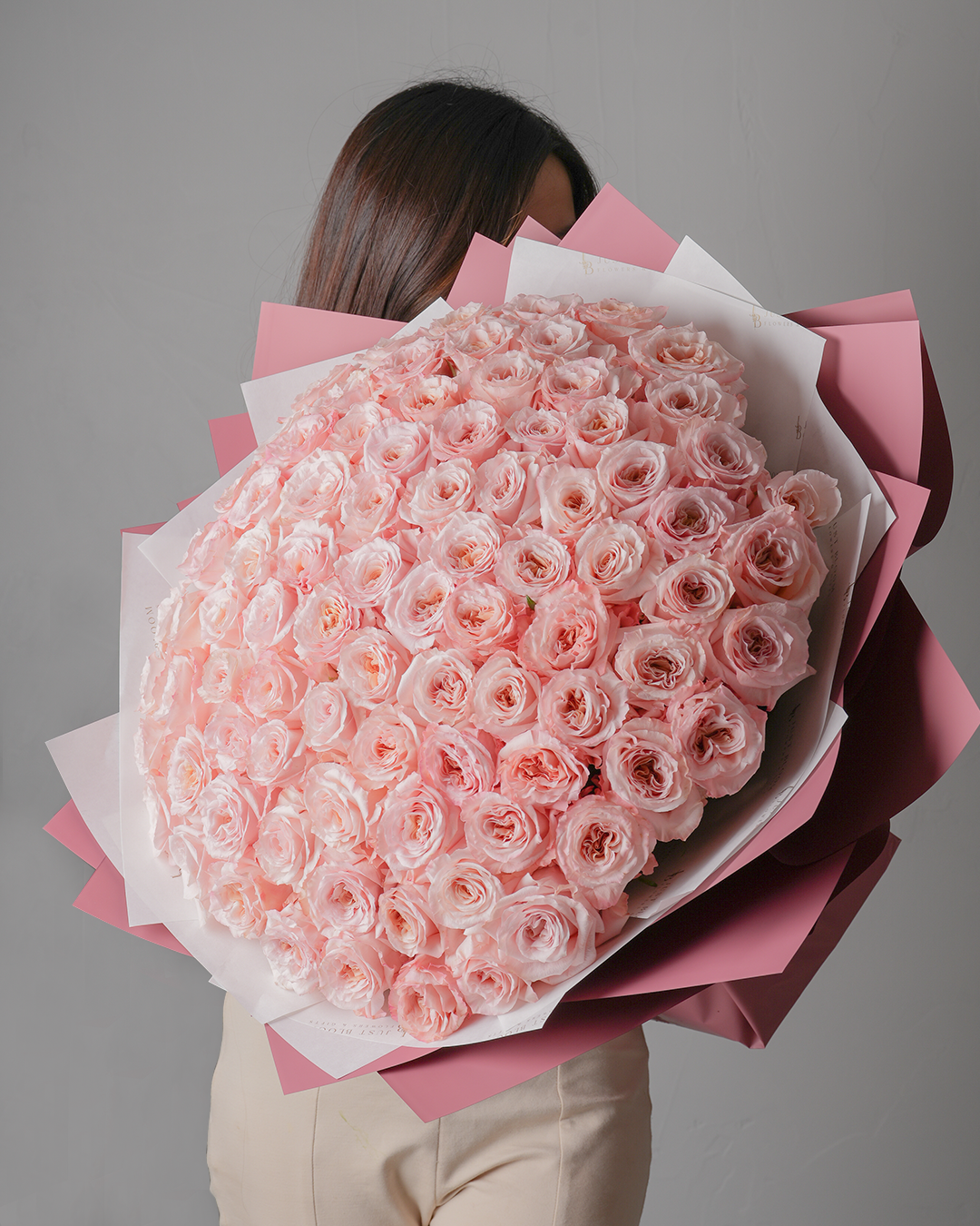 Woman holding Arabella grand pink rose bouquet wrapped in pink and white paper