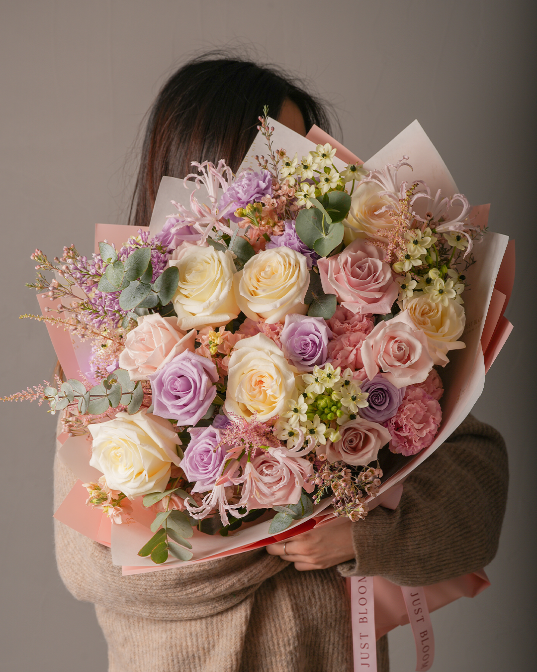 Lauren pink purple mixed rose bouquet with star of Bethlehem held by woman in beige sweater