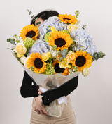 Blue and yellow tone bouquet with sunflowers, roses, stocks, hydrangeas, viburnums, eustomas, and eucalyptus."