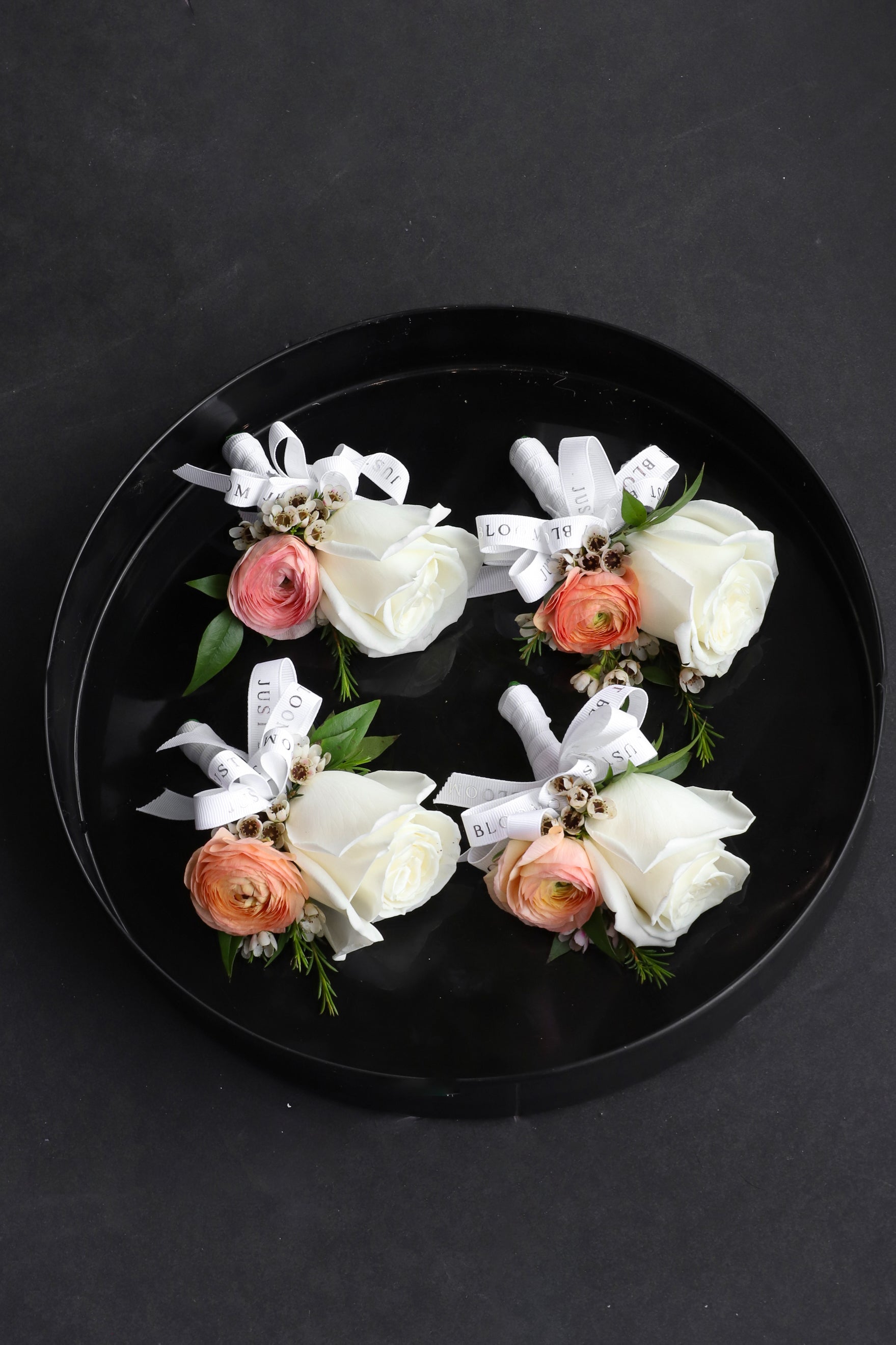 Close-up of four Dear One wedding corsages on a black tray by Just Bloom Hong Kong, showcasing ivory roses, peach ranunculus and wintersweet with fresh foliage